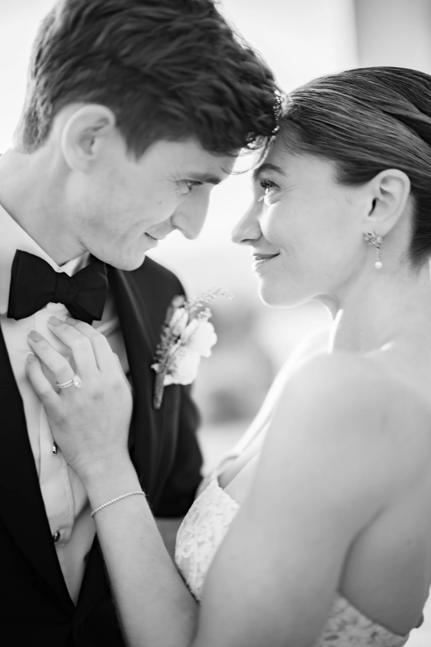 Black and white photo of a bride and groom with foreheads touching, smiling, and looking into each other's eyes.