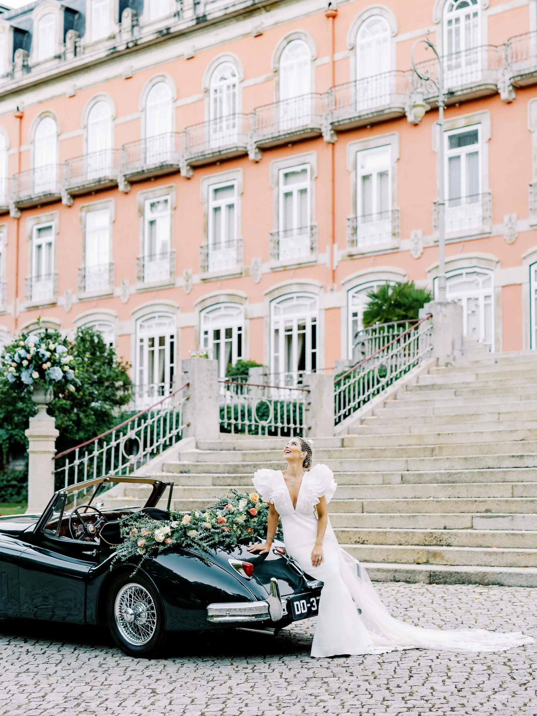 Bride by a vintage car in front of the staircase at Vidago Palace in Portugal