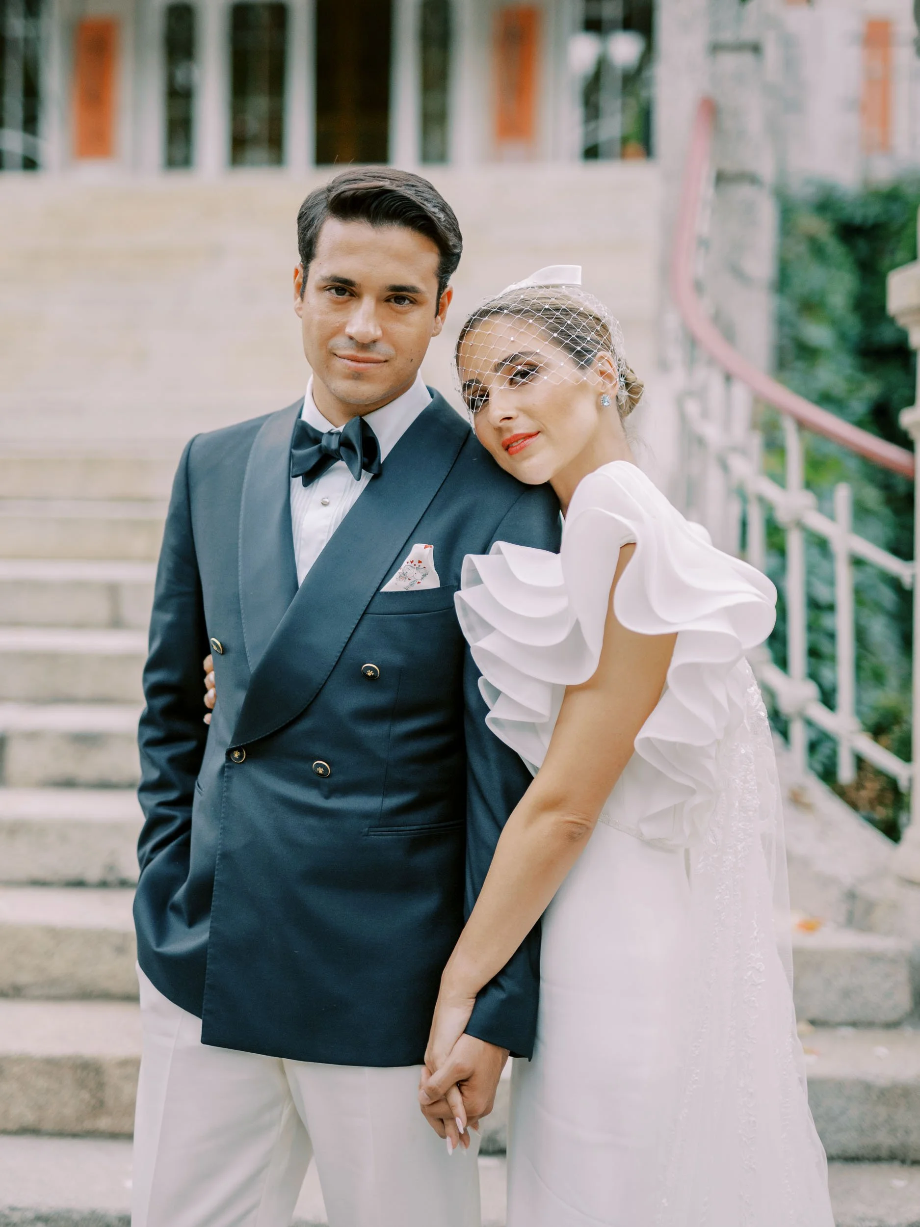 A couple dressed in wedding attire, holding hands, standing on outdoor steps with a building in the background at Vidago Palace