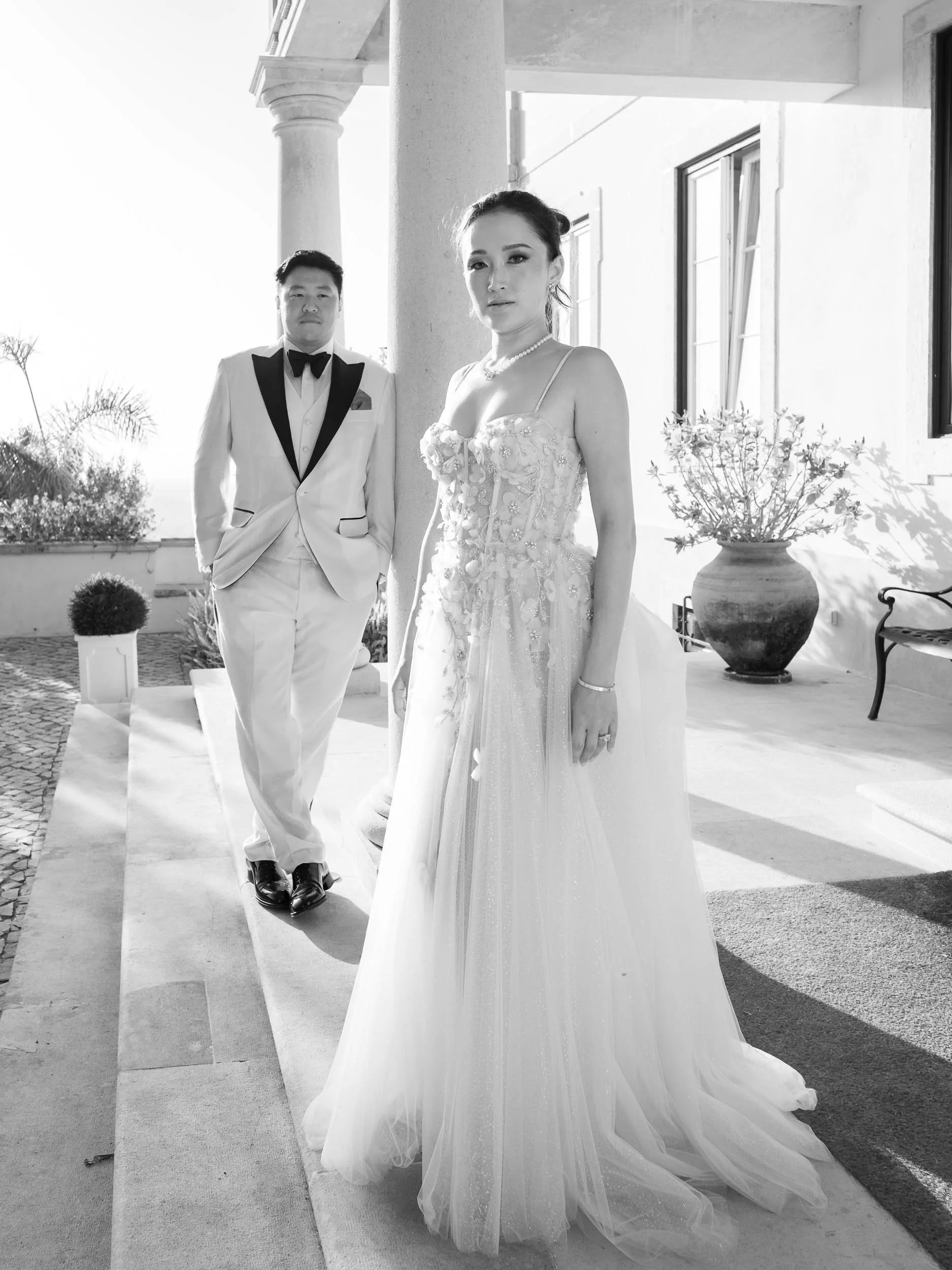 A bride in a wedding dress standing outside with a groom dressed in a tuxedo behind her at Quinta da Bella Vista Palace in Sintra