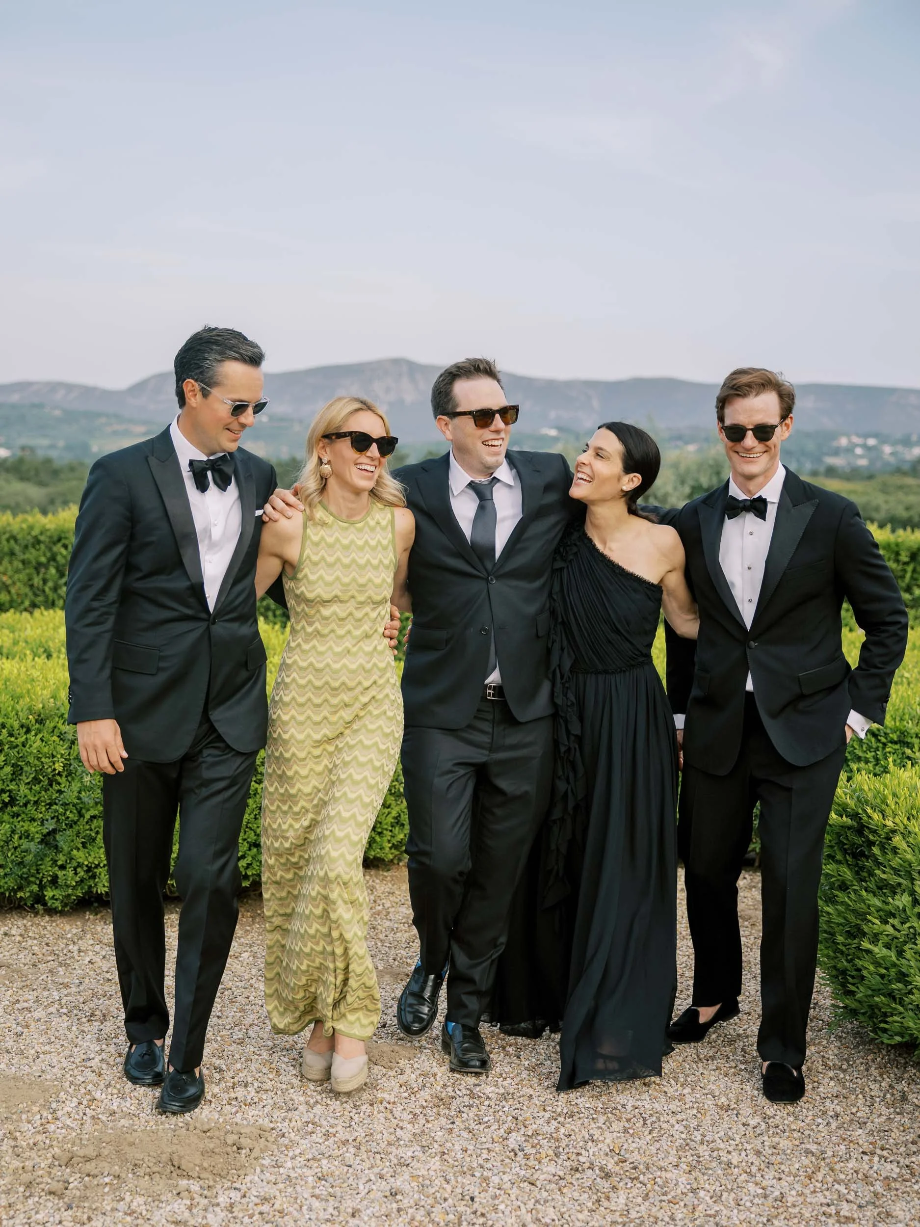 A group of five wedding guests dressed in formal attire walking together outdoors, smiling, with mountains and greenery in the background at Herdade do Perú in Portugal