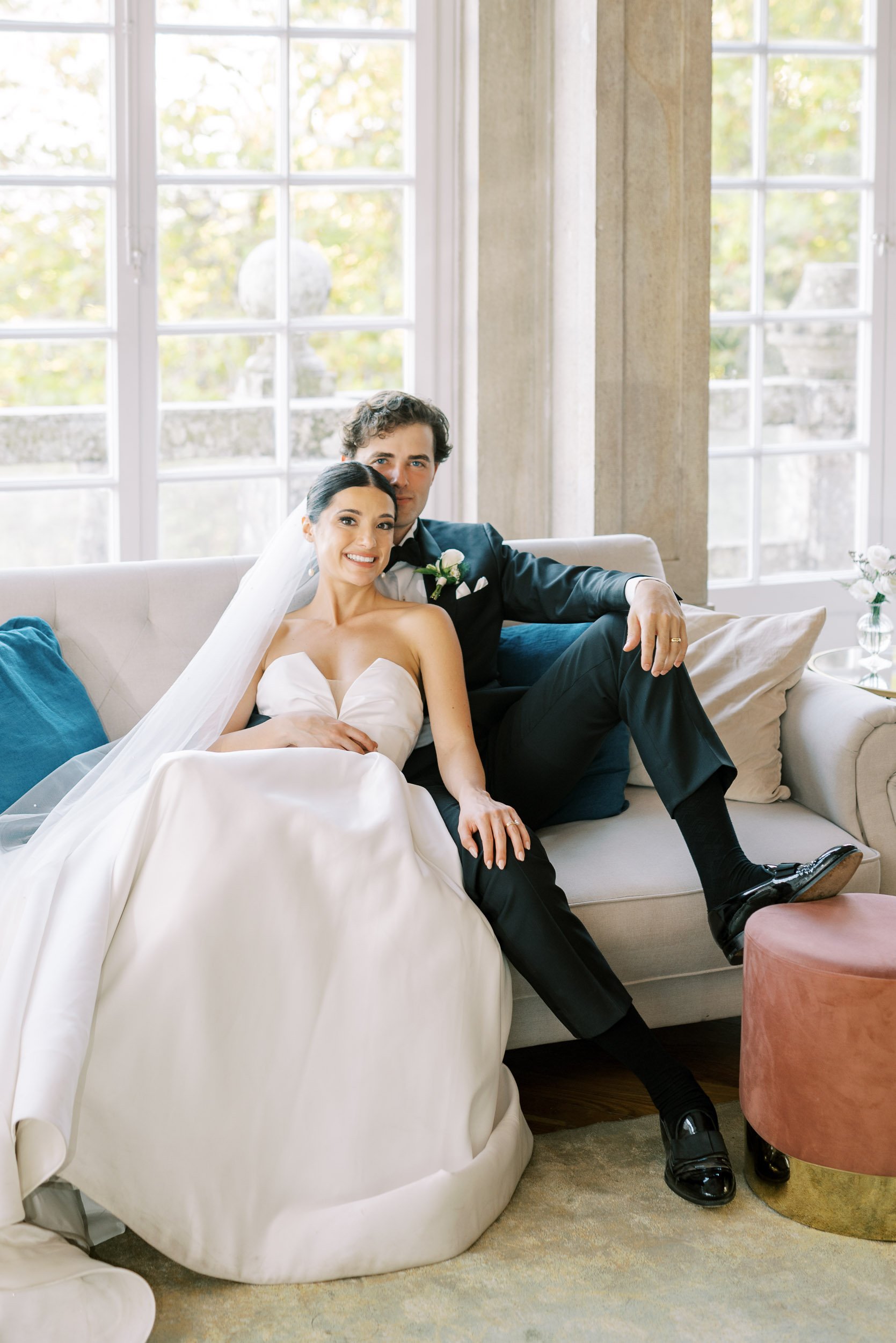 Bride and Groom sitting on a sofa, smiling, in a bright room with large windows and outdoors view at Casa dos Penedos