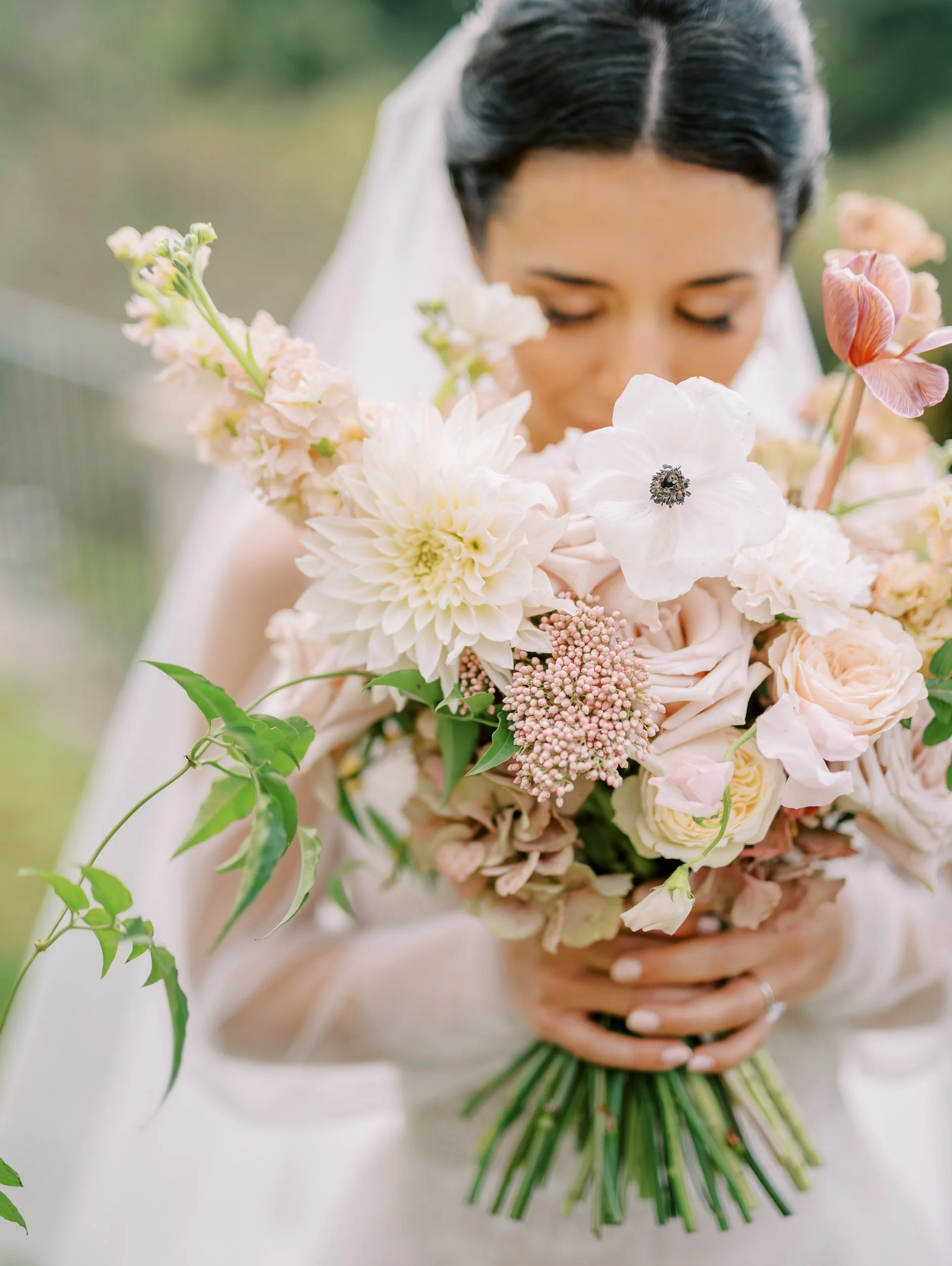 A bride holding a bouquet of pink and white flowers, with her eyes closed and head bowed.
