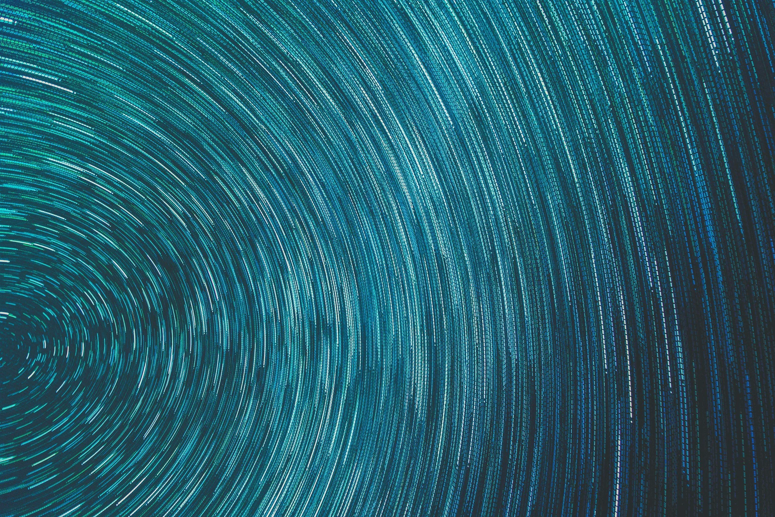 Abstract digital art with concentric circles made of small glowing blue and turquoise lines on a dark background.