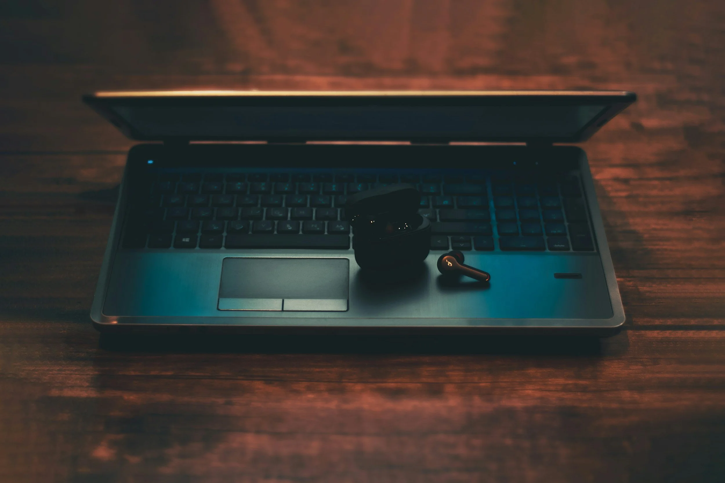 Open laptop on a wooden surface with a black wireless earbud.