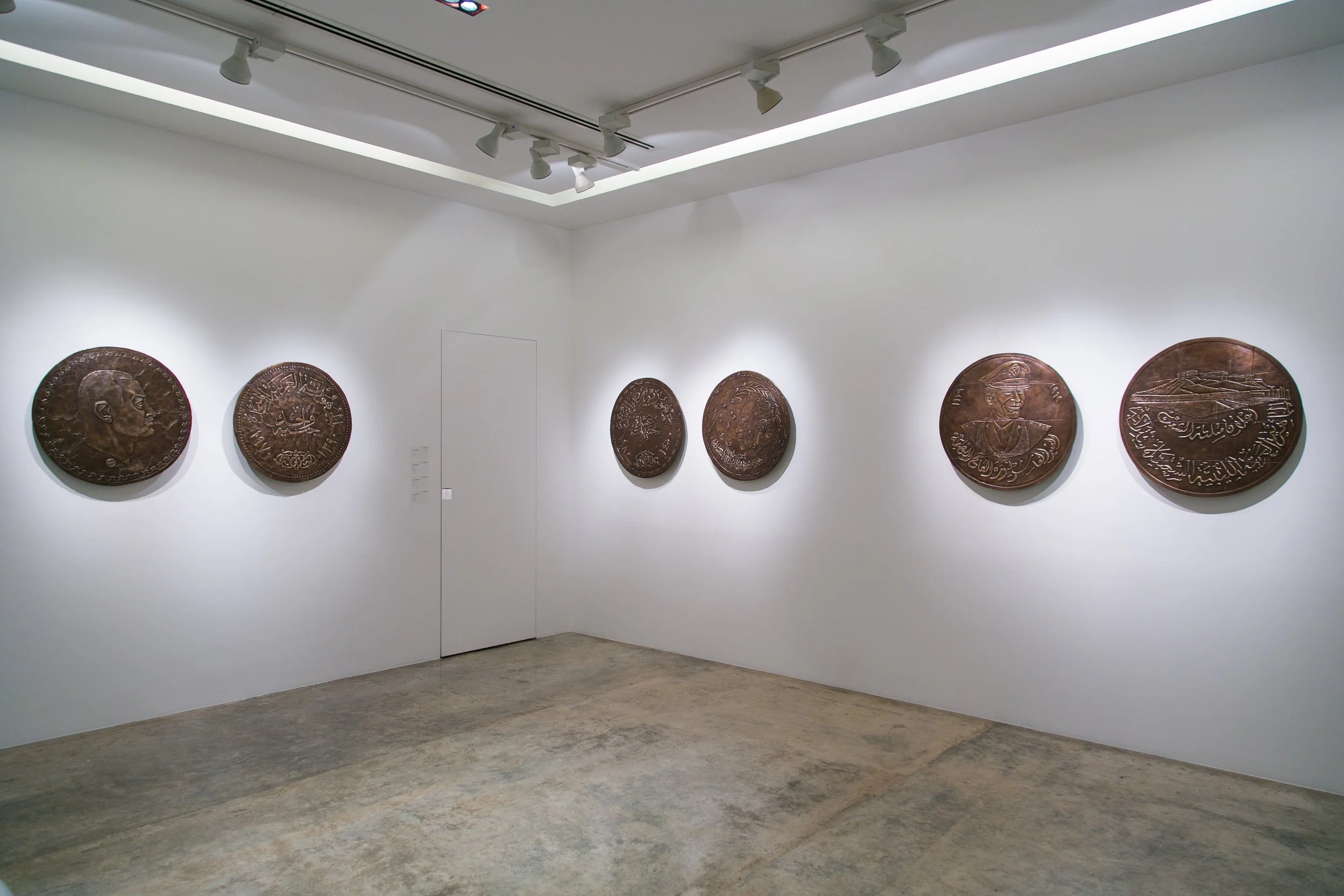 Gallery with large round bronze plaques on white walls, depicting various portraits, symbols, and Arabic script.
