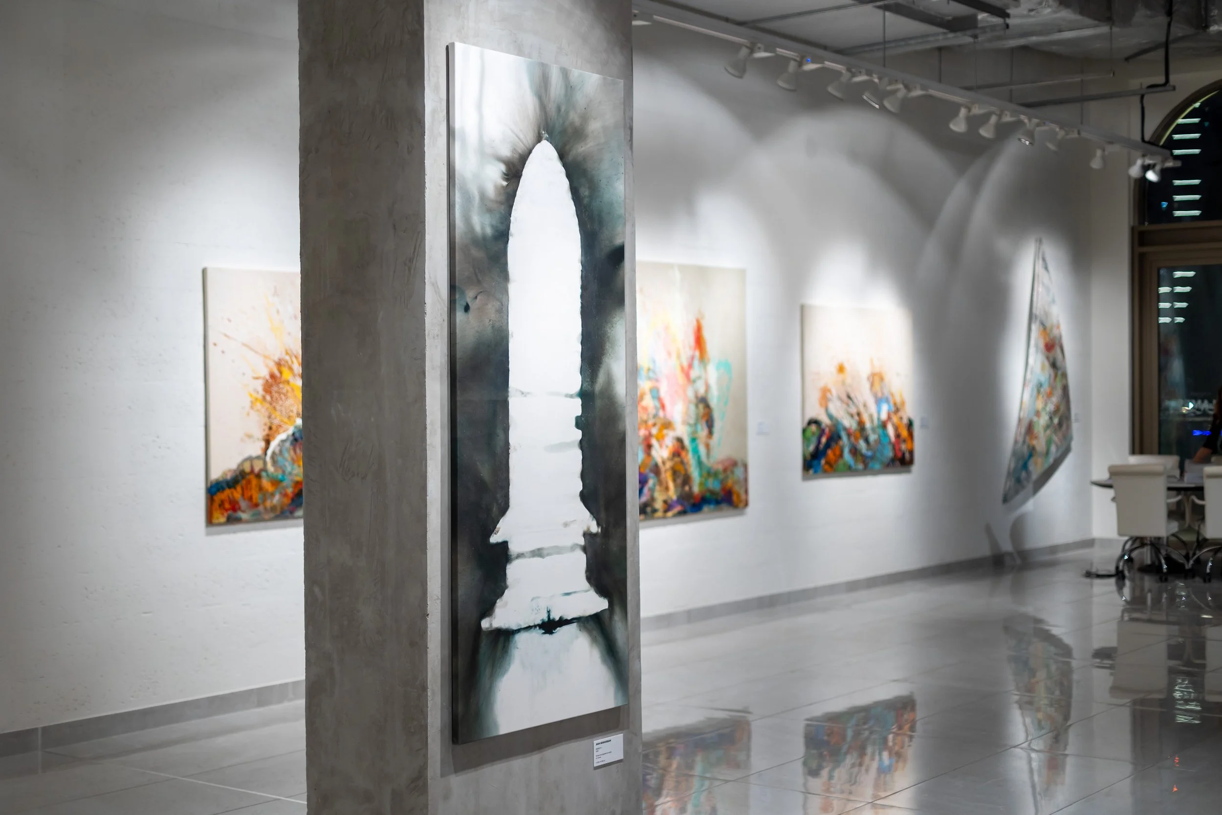 Contemporary art gallery displaying abstract paintings on white walls, with spot lighting and a polished floor.
