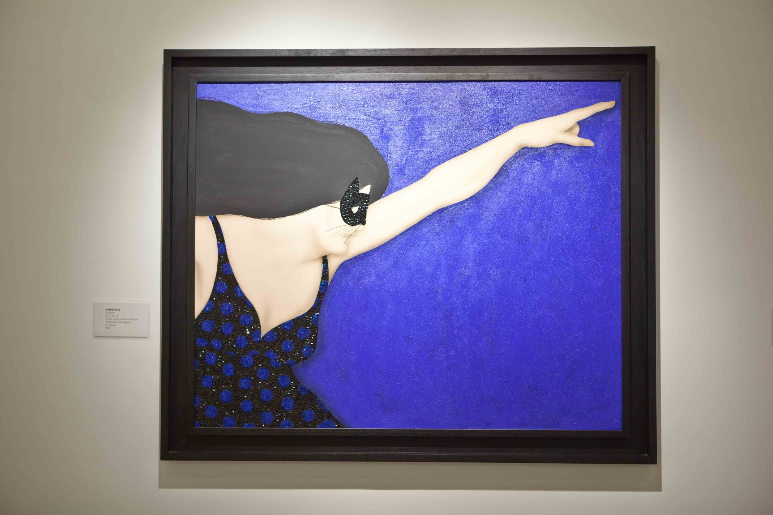 Painting of a woman with long black hair, wearing sunglasses and a dress with blue polka dots, pointing her right arm outward against a blue background.