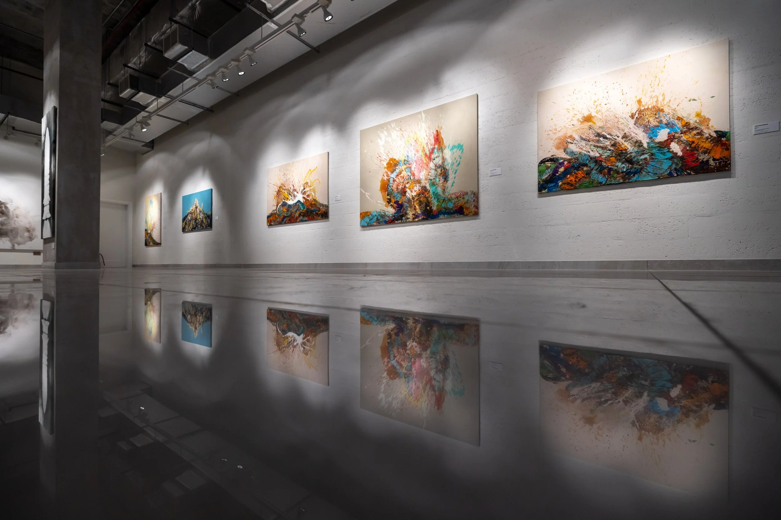 Art gallery with abstract colorful paintings on white walls, reflected on a shiny floor.