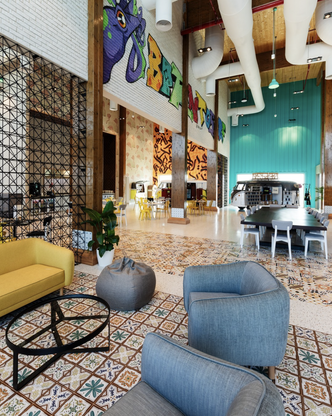 An interior view of a colorful, modern hotel lobby with a mix of seating, including a yellow sofa, blue armchairs, and a round gray pouf. The floor is decorated with patterned tiles, and the walls feature vibrant murals and graffiti-style art. There 