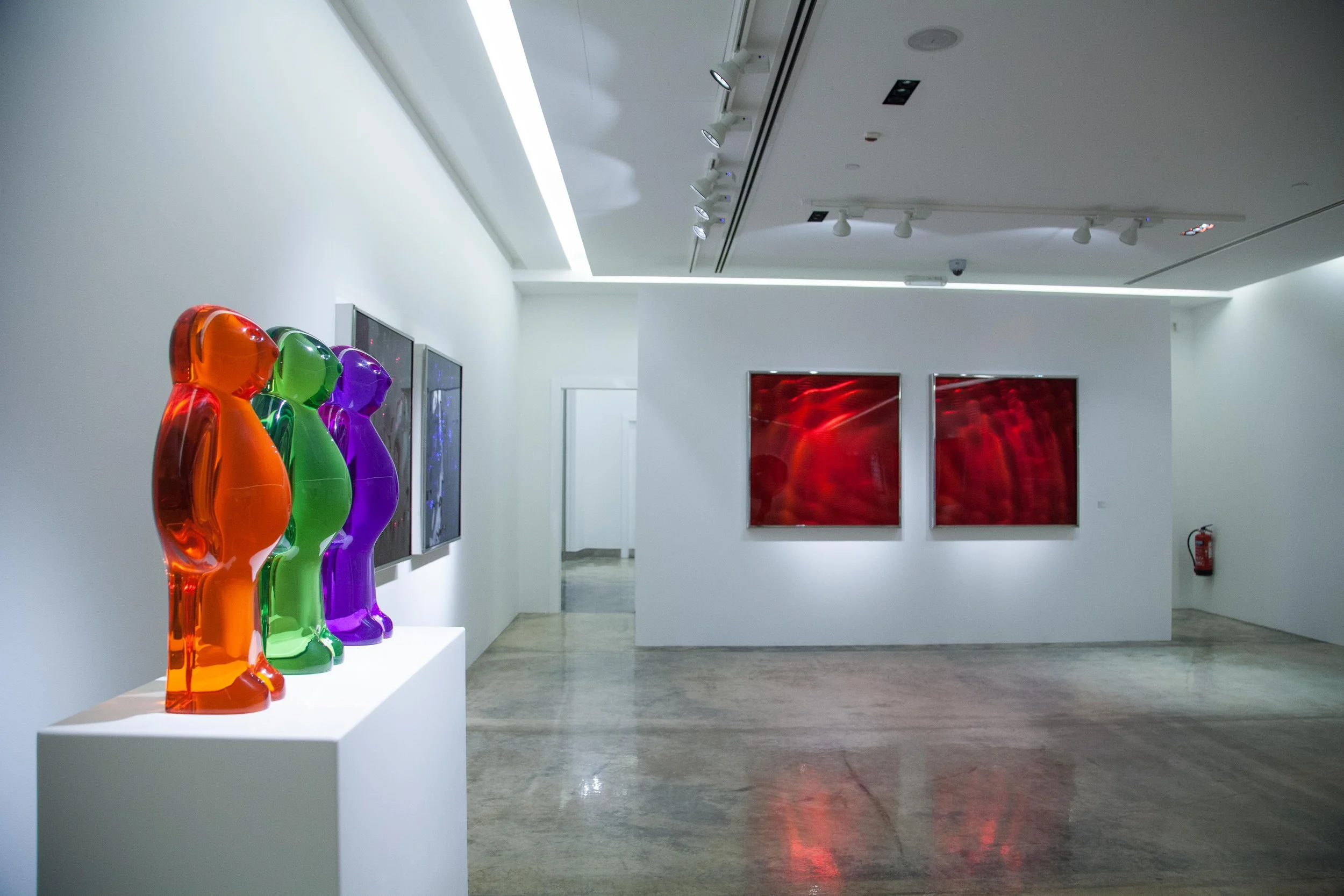 Art gallery interior with colorful glass bear sculptures on a pedestal, and red abstract paintings on the wall.