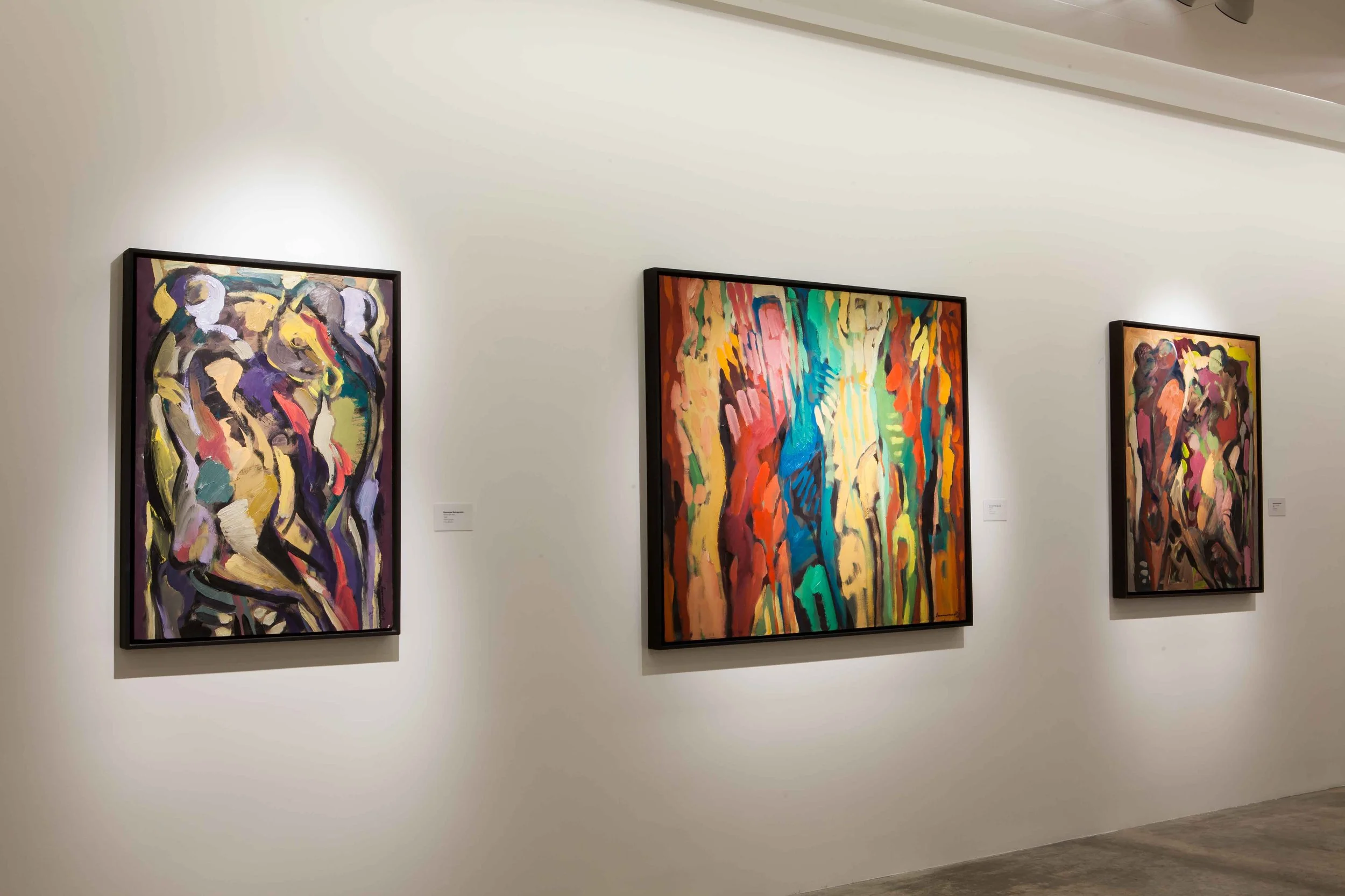 Three abstract colorful paintings hanging on a white gallery wall in an art museum.