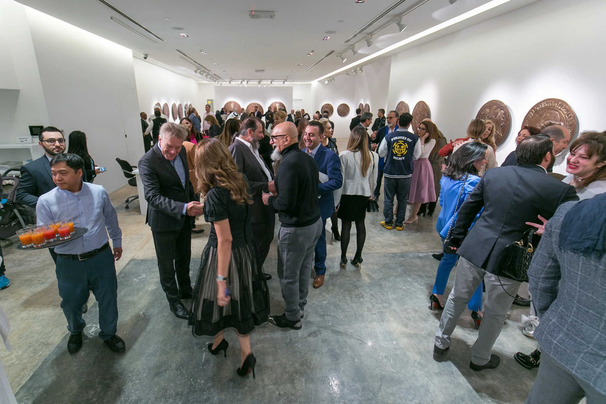 People socializing in an art gallery with large bronze plaques on white walls.