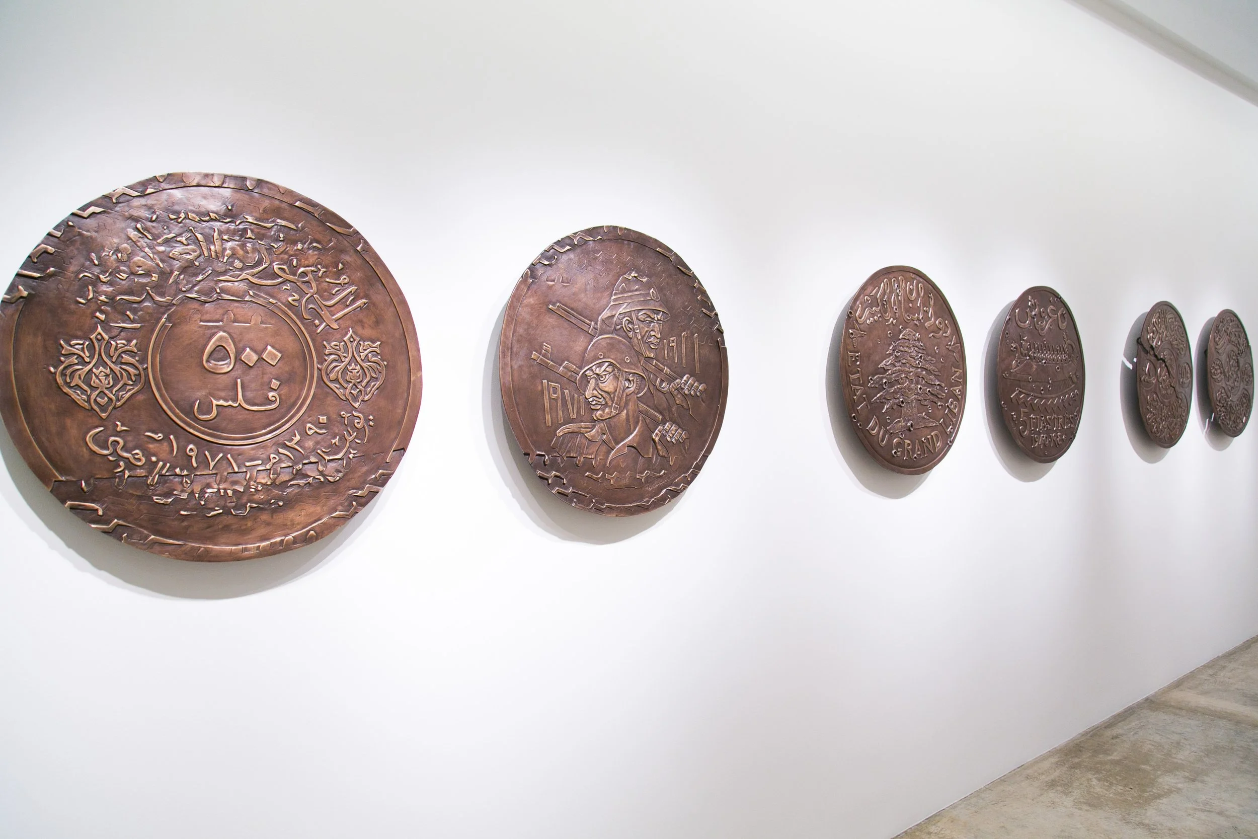 Exhibition of circular metallic plaques with engraved designs on a white gallery wall.