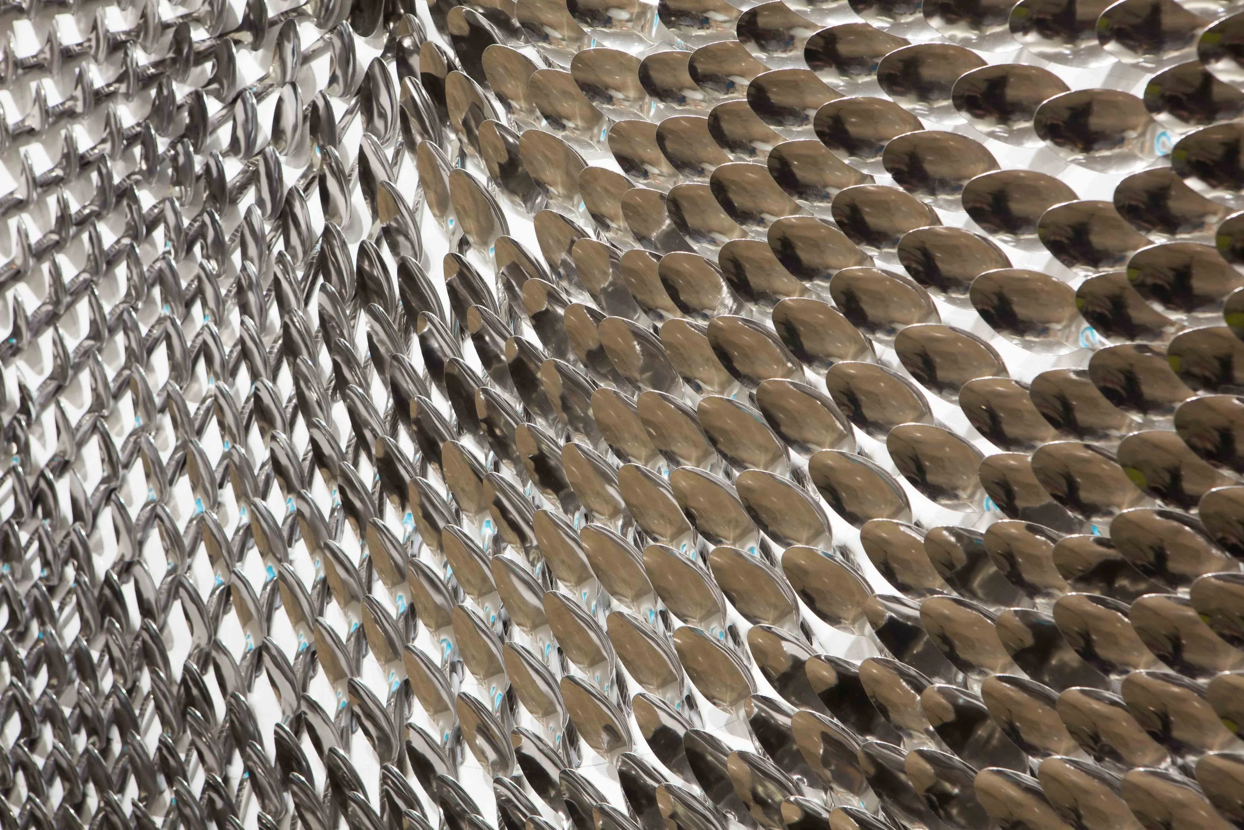 Close-up of a wall made of overlapping metallic spoons arranged in a pattern.
