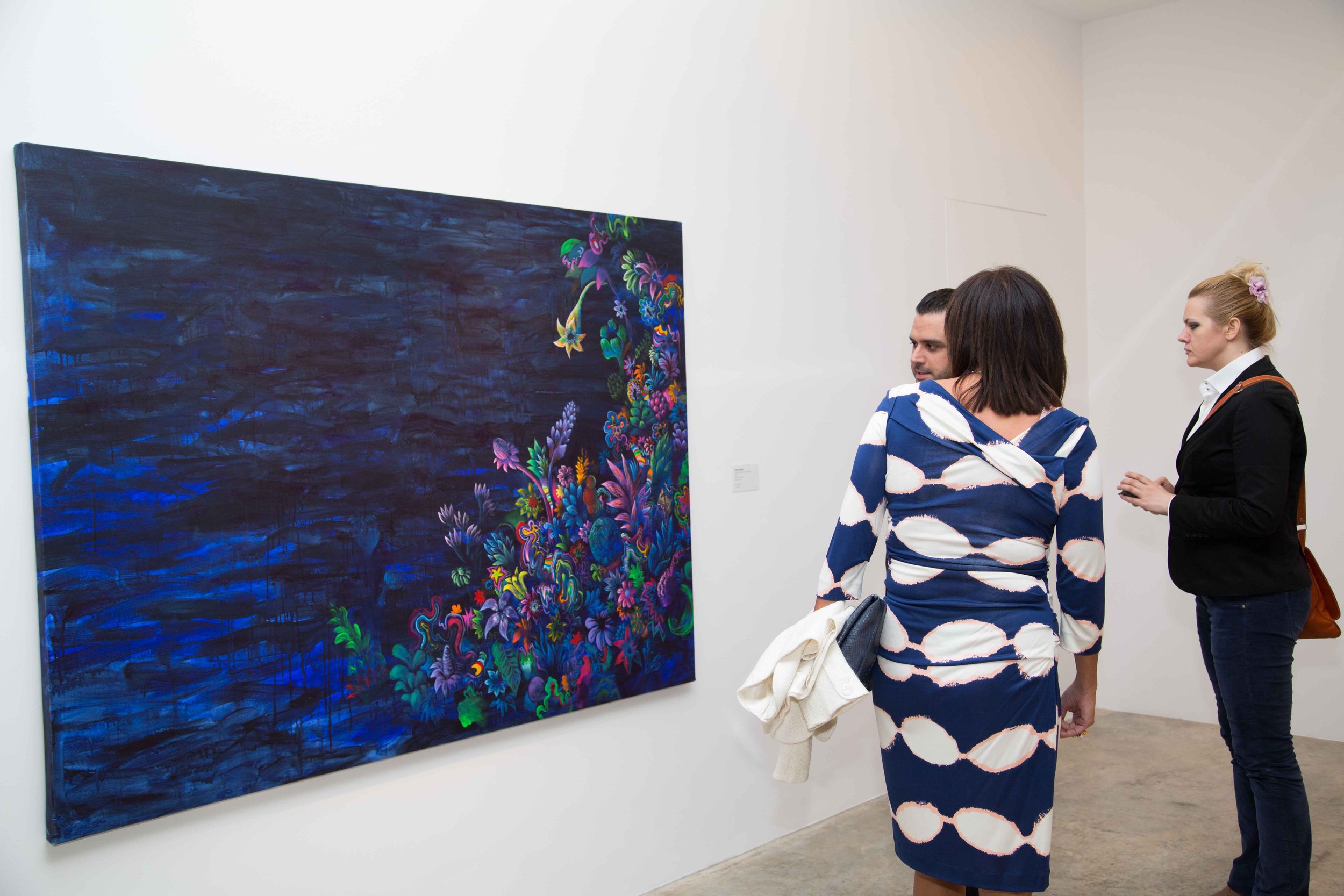 Three people viewing a large colorful abstract painting at an art gallery.