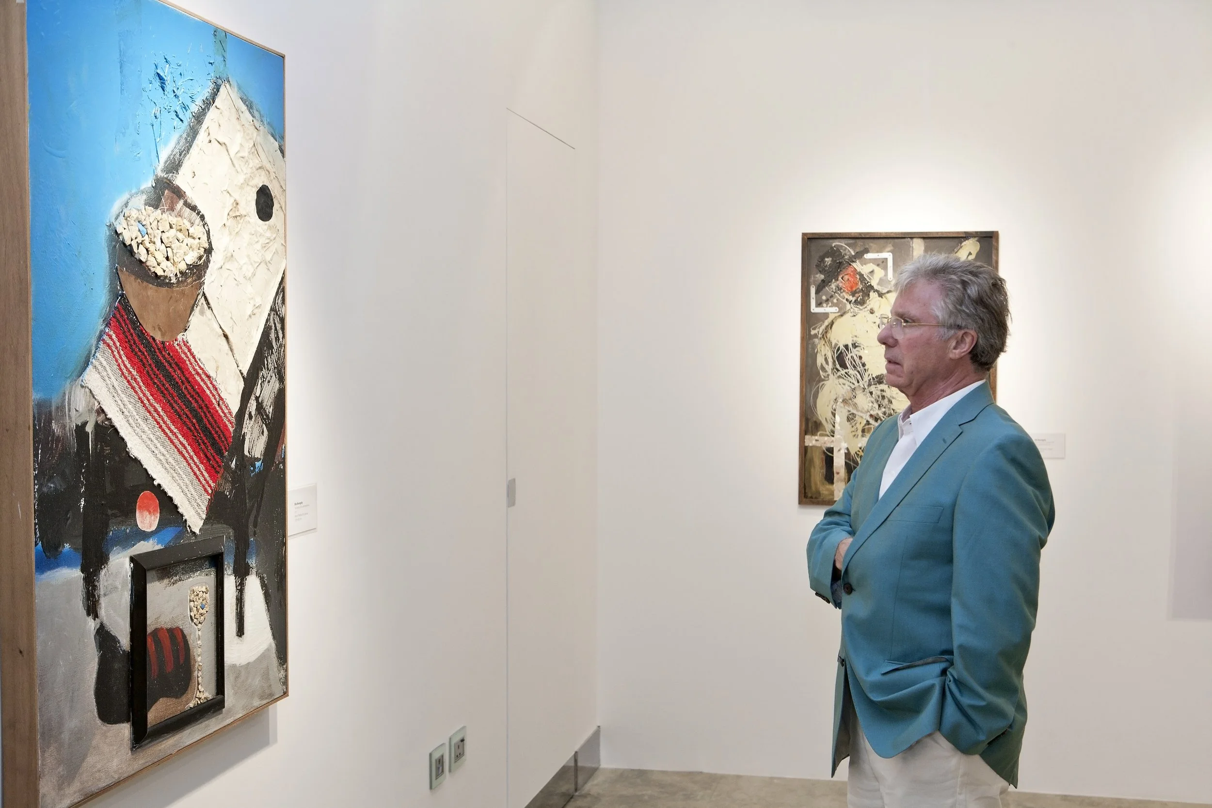 A man in a teal blazer and white shirt observing abstract artwork in a gallery.