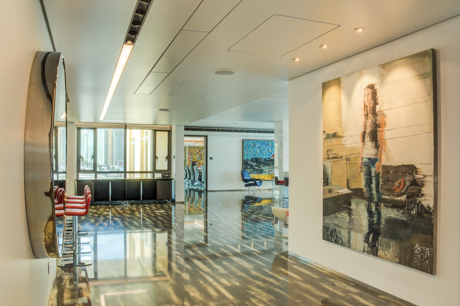 Interior of a modern art gallery or lounge with abstract paintings on the walls, chairs, and large windows letting in natural light.