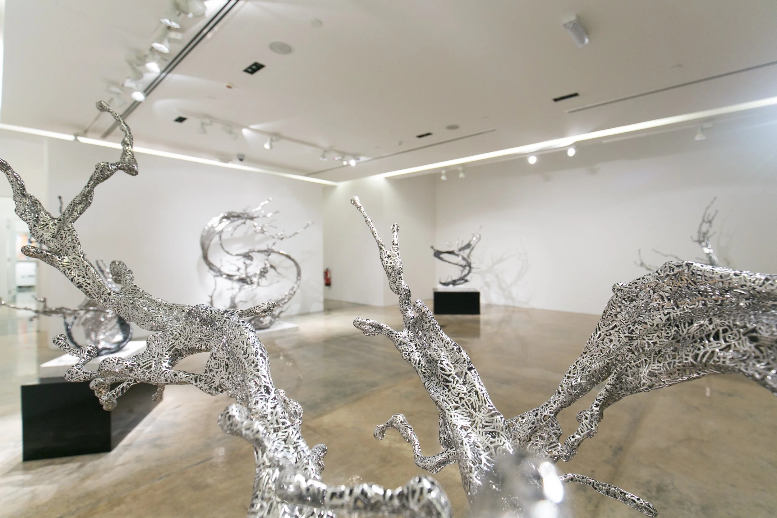 Modern art sculptures resembling distorted silver tree branches in an art gallery with white walls and overhead lighting