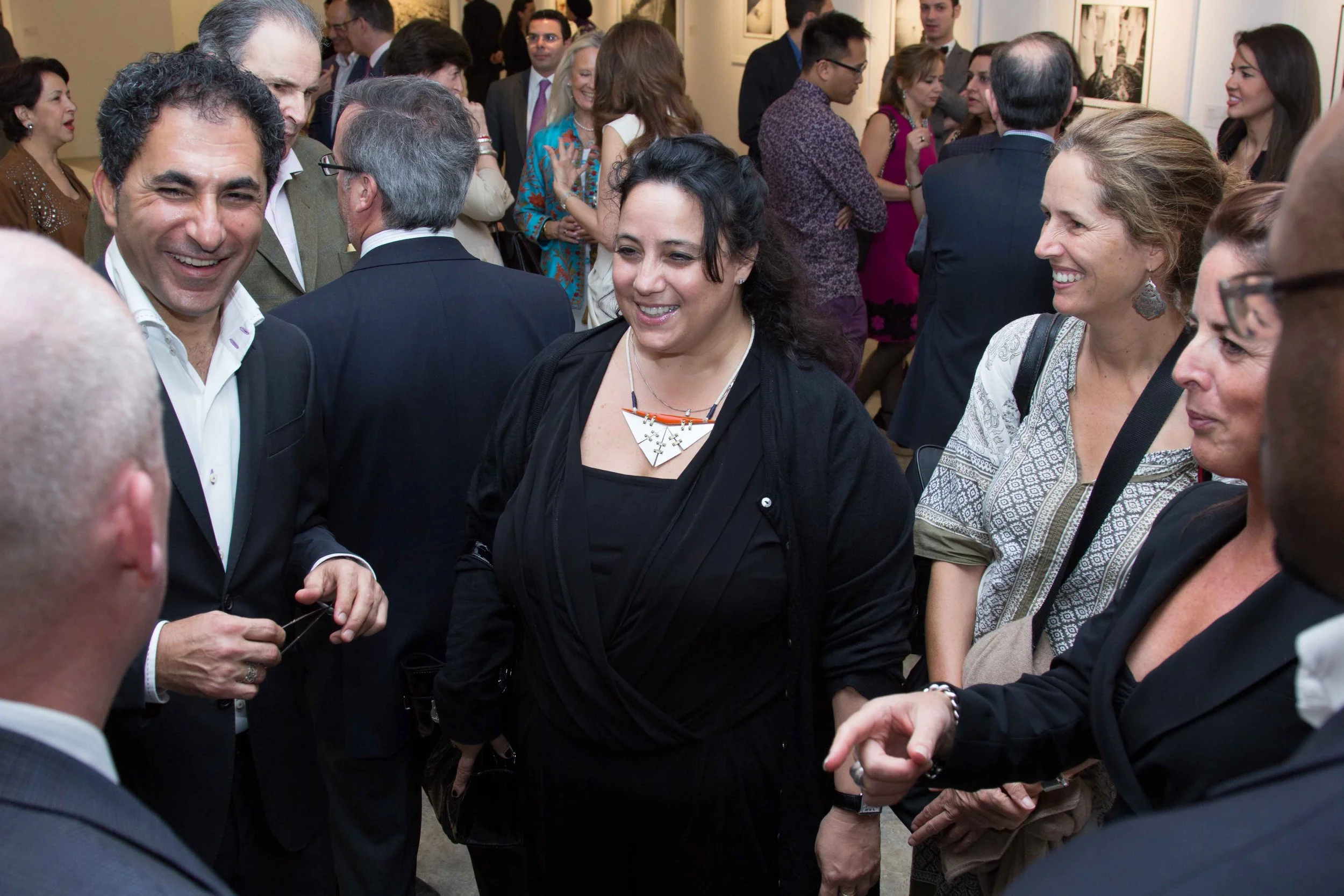 Group of people at a social event, engaged in conversation, smiling, in an art gallery or similar setting.