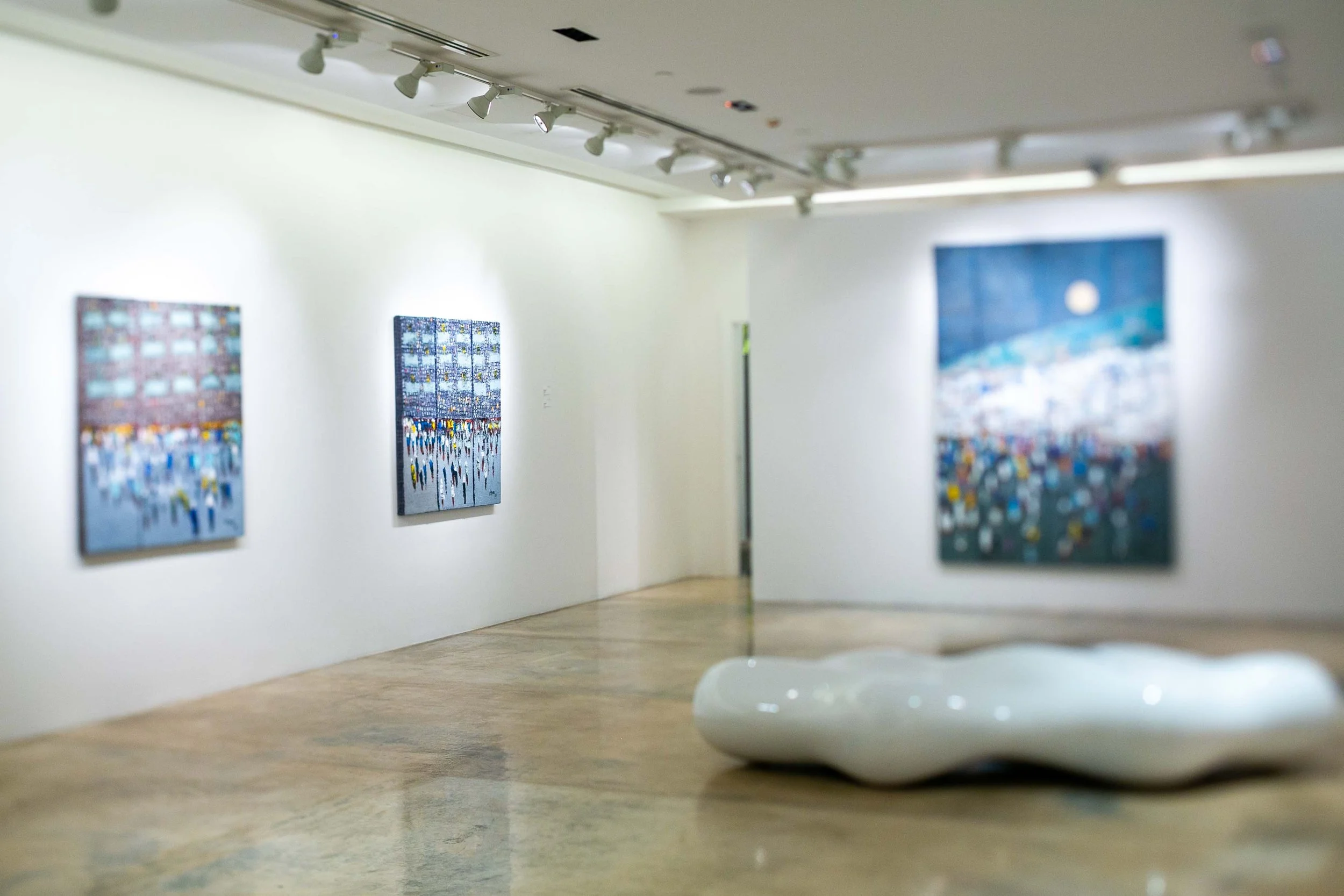 Art gallery with three paintings on a white wall and a white abstract sculpture on the polished floor.