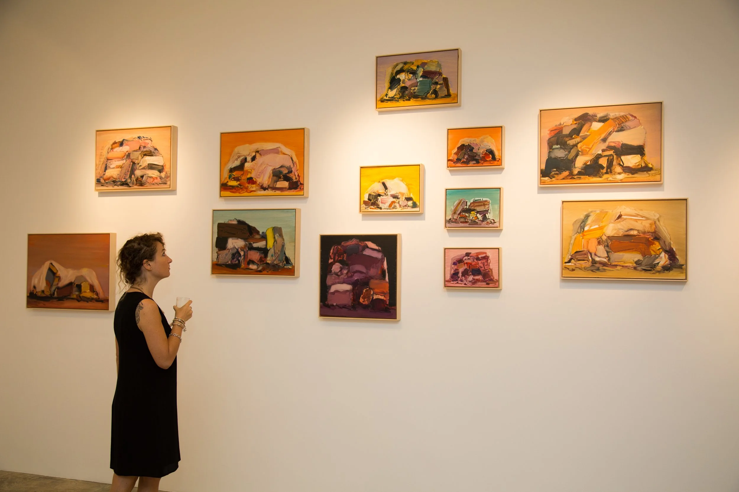 A woman in a black dress looking at abstract paintings in a gallery