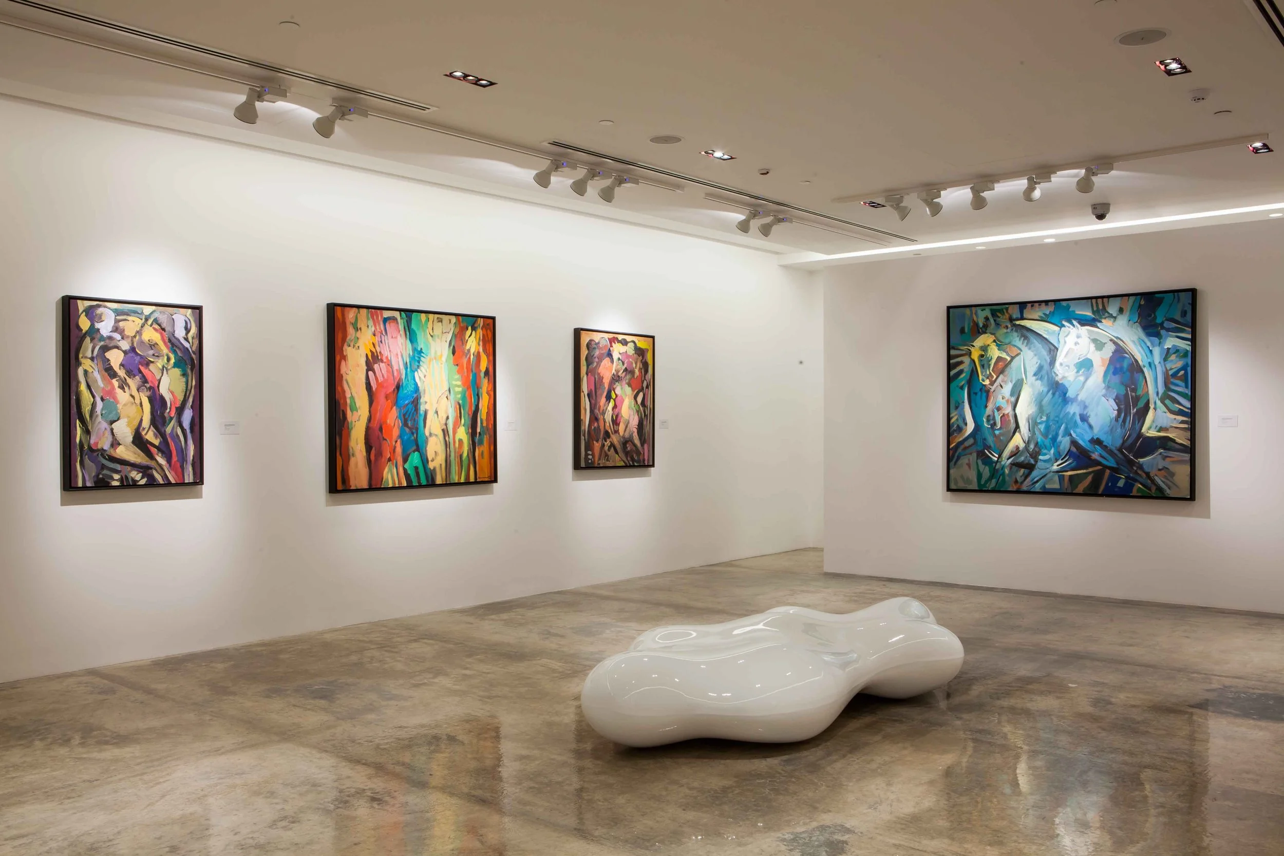 Art gallery with four colorful abstract paintings on white walls and a white sculptural bench in the center.