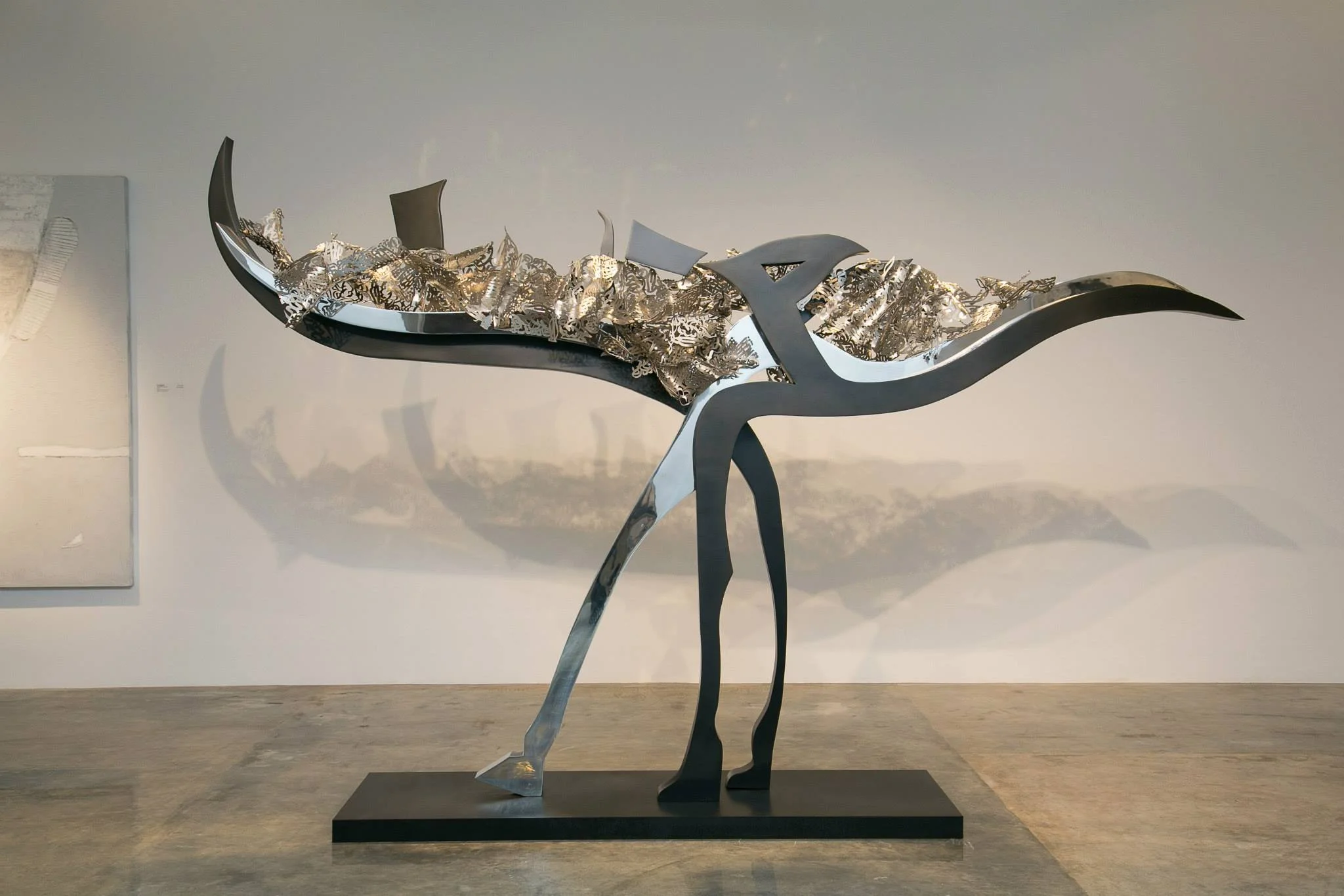 Modern sculpture of a whale with a black and silver color scheme, mounted on a black base.
