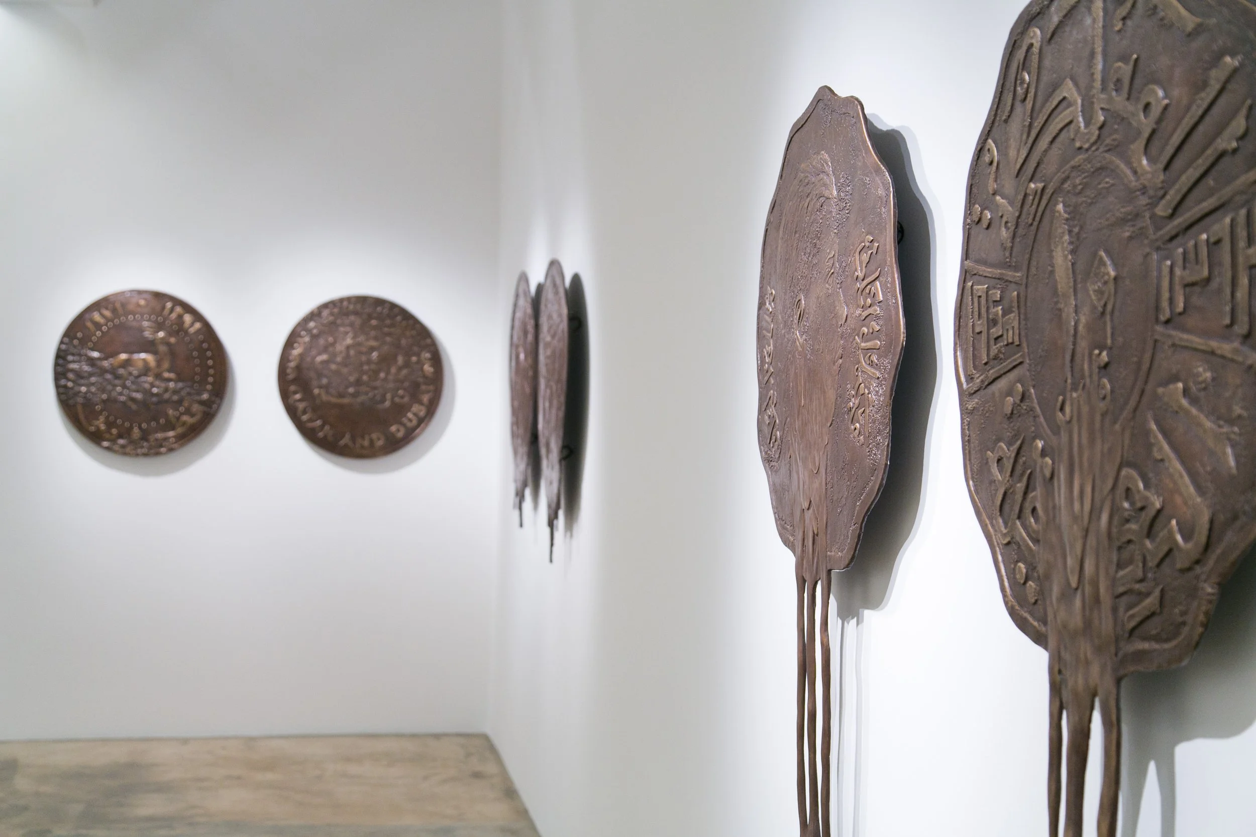 A gallery wall with bronze plaques and coins, arranged in a row on a white wall.