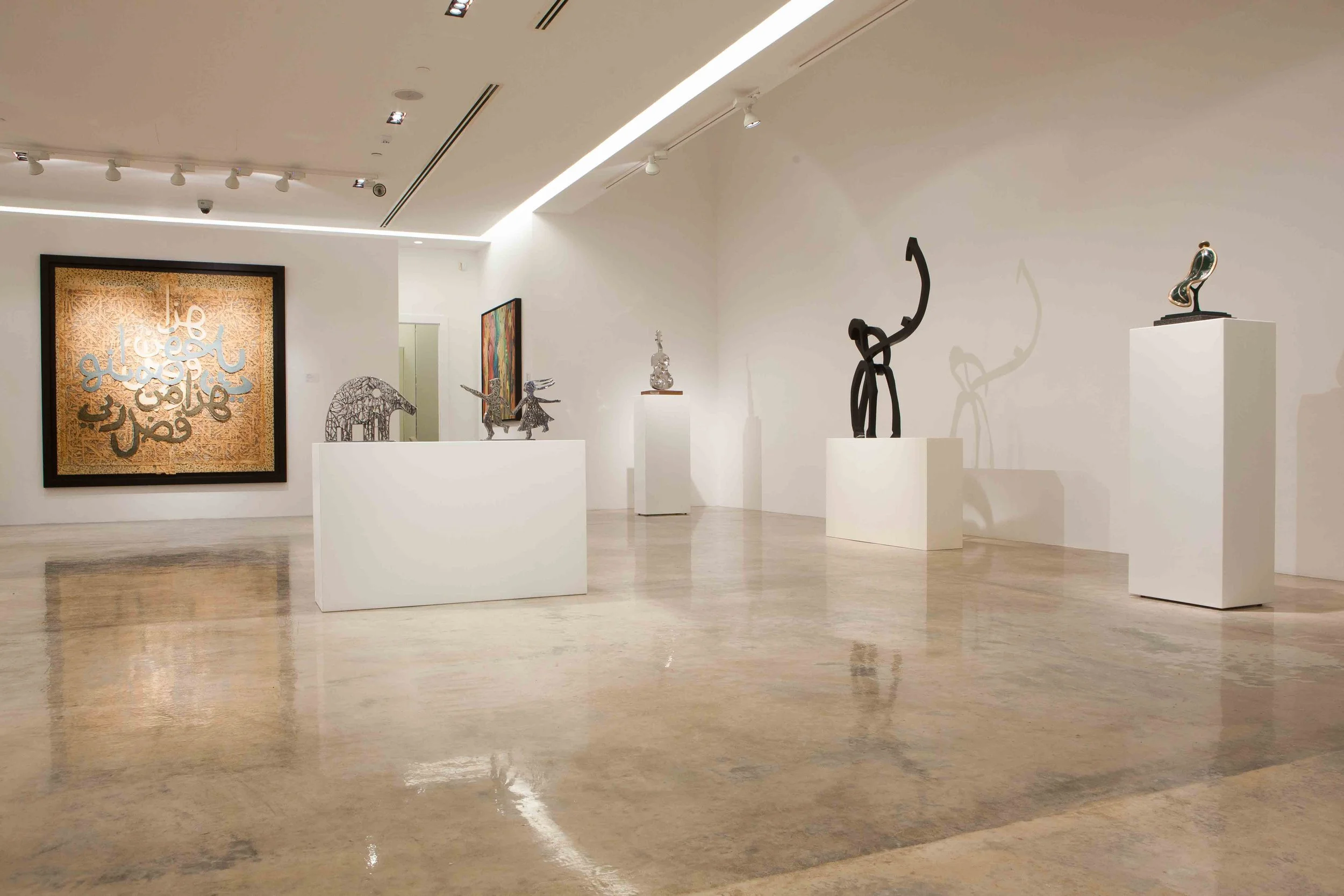 Art gallery with sculptures on white pedestals and framed artwork on white walls.