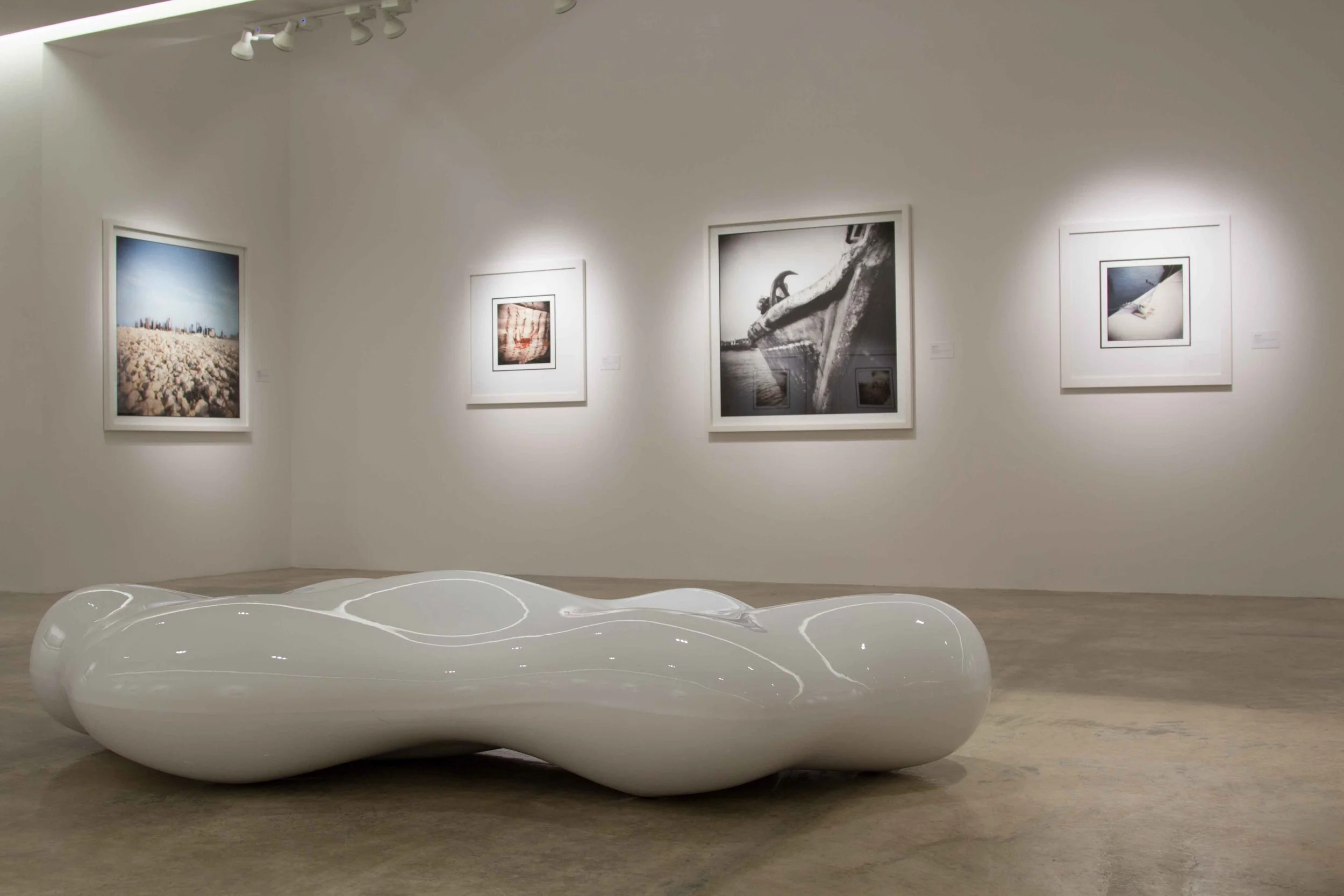 An art gallery with four framed photographs on white walls and a modern, abstract white sculpture on the floor.