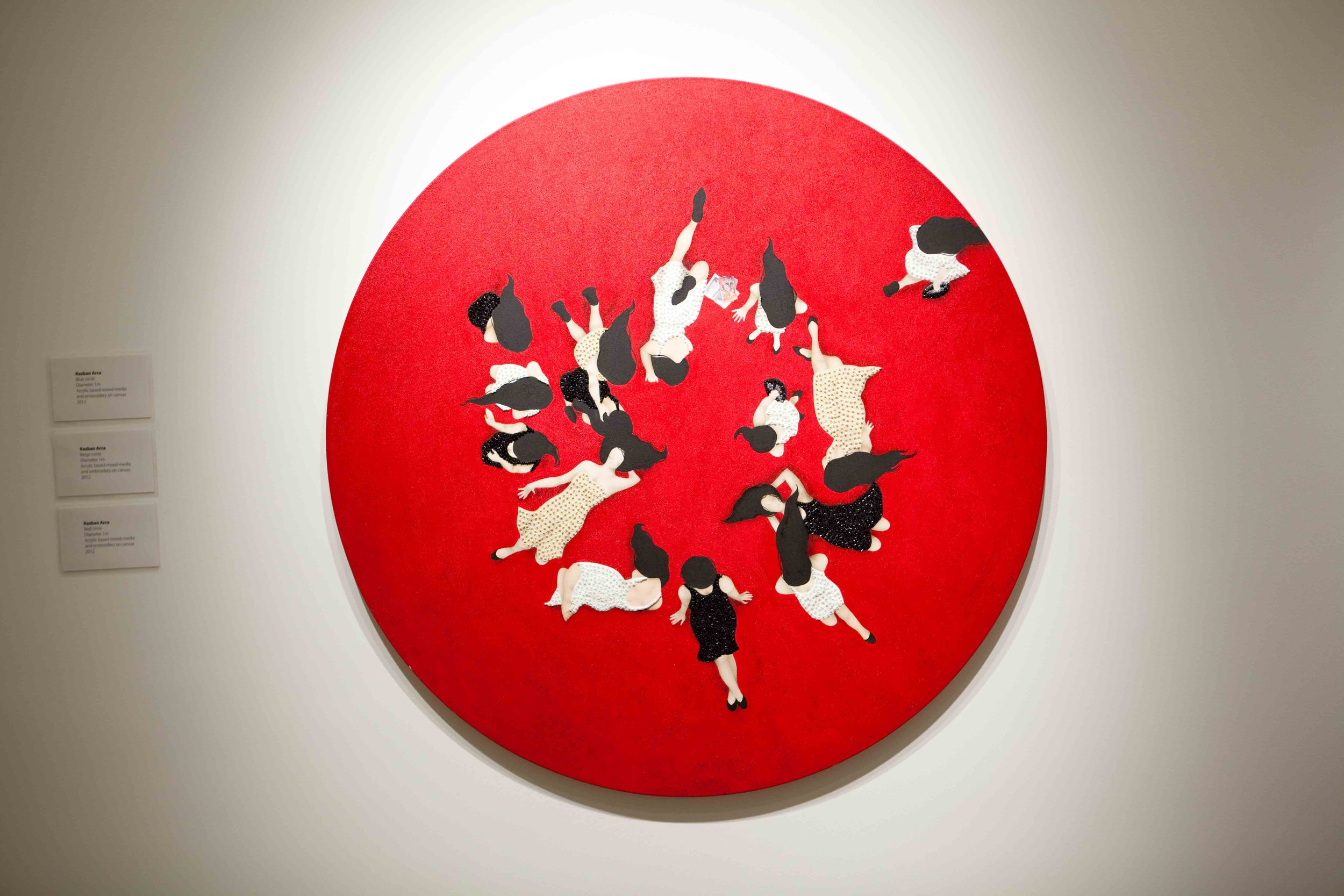 An art piece with silhouettes of women in dresses arranged in a circle on a red background.