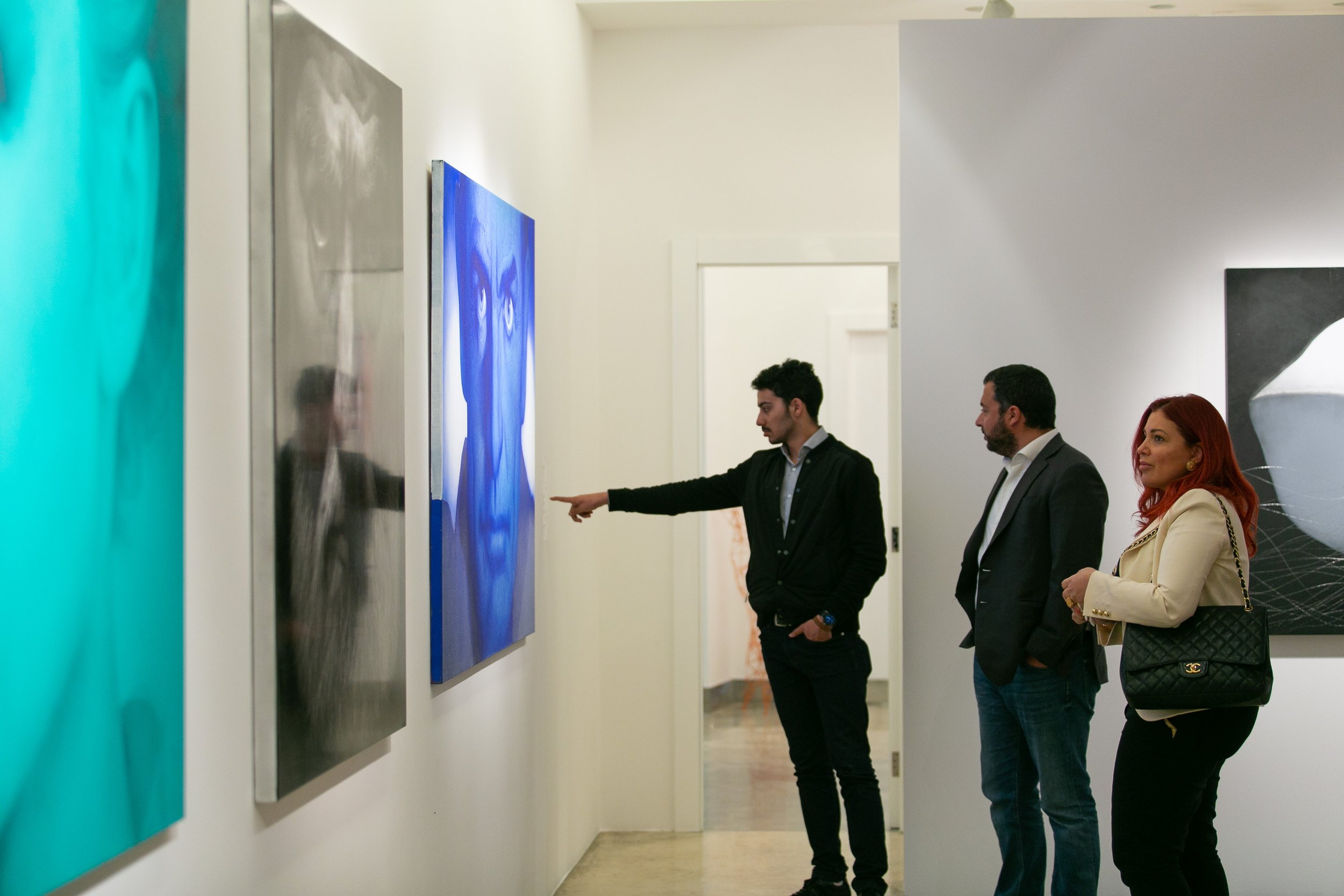 Three people observing abstract artwork in an art gallery, one person pointing at the painting on the wall.