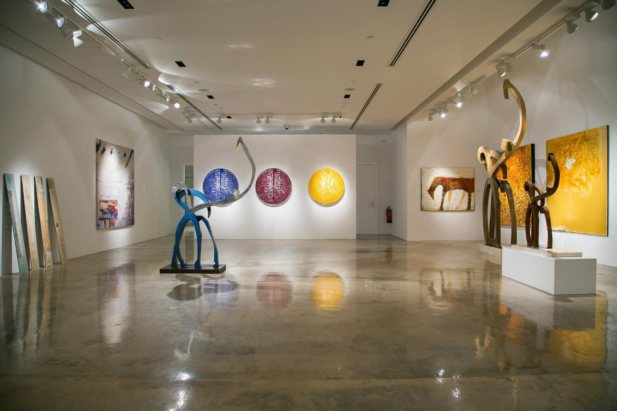 An art gallery with various sculptures and paintings displayed on white walls, including abstract paintings and colorful sculptures.