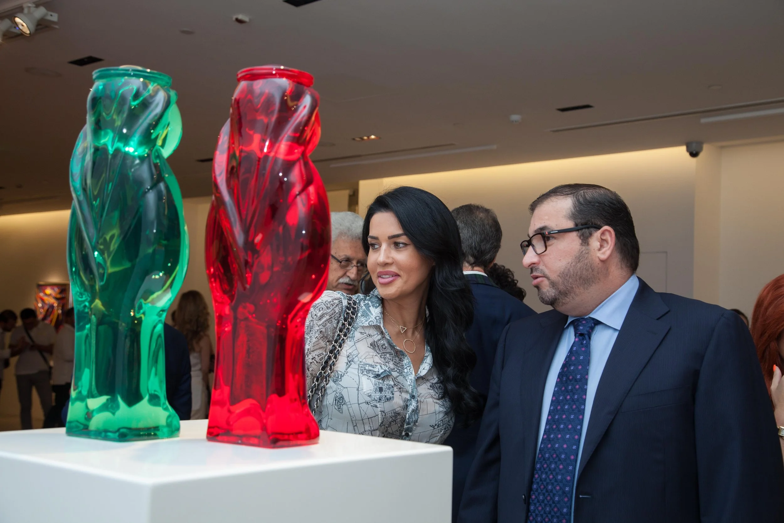 People observing colorful sculptural glass art pieces at an art exhibition.