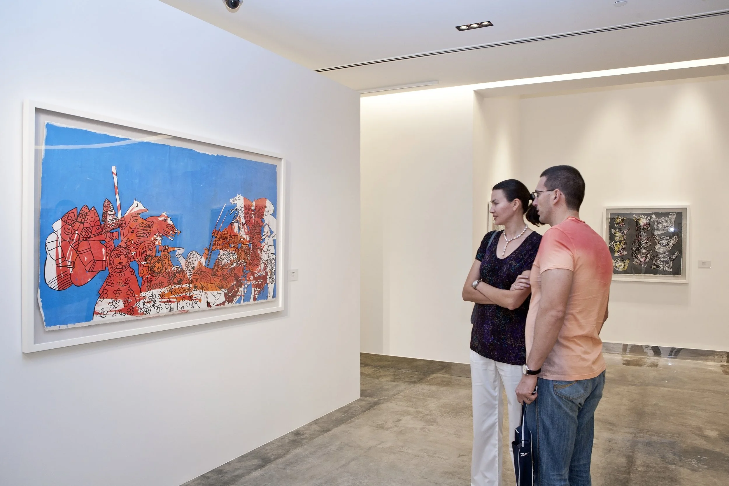 Two people viewing artwork in a gallery, one woman and one man, standing in front of a colorful abstract painting on a white wall.