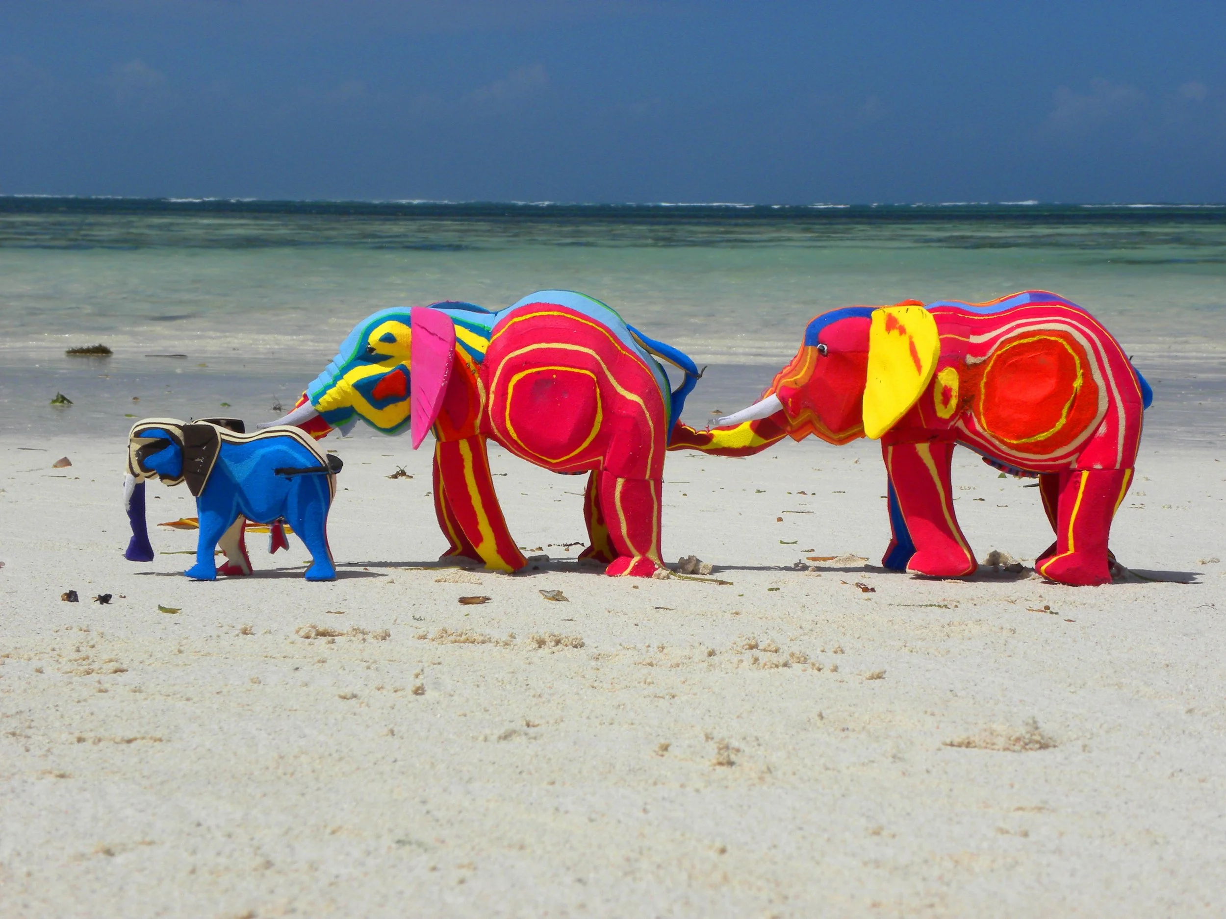 Colorful plush elephant toys on the sandy beach, with the ocean and sky in the background.