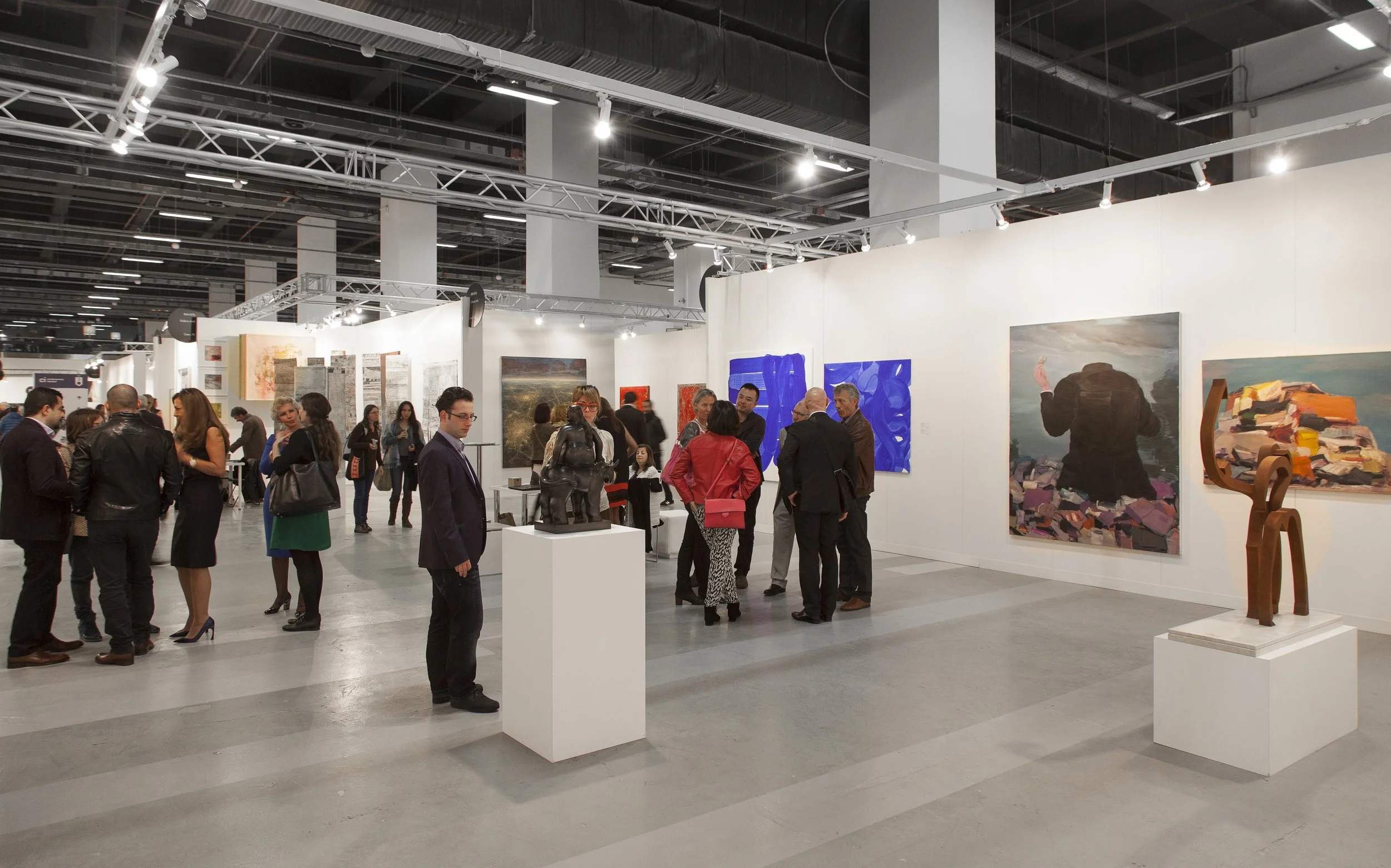 People viewing artwork and sculptures at an art gallery or museum exhibition with white walls and modern lighting.