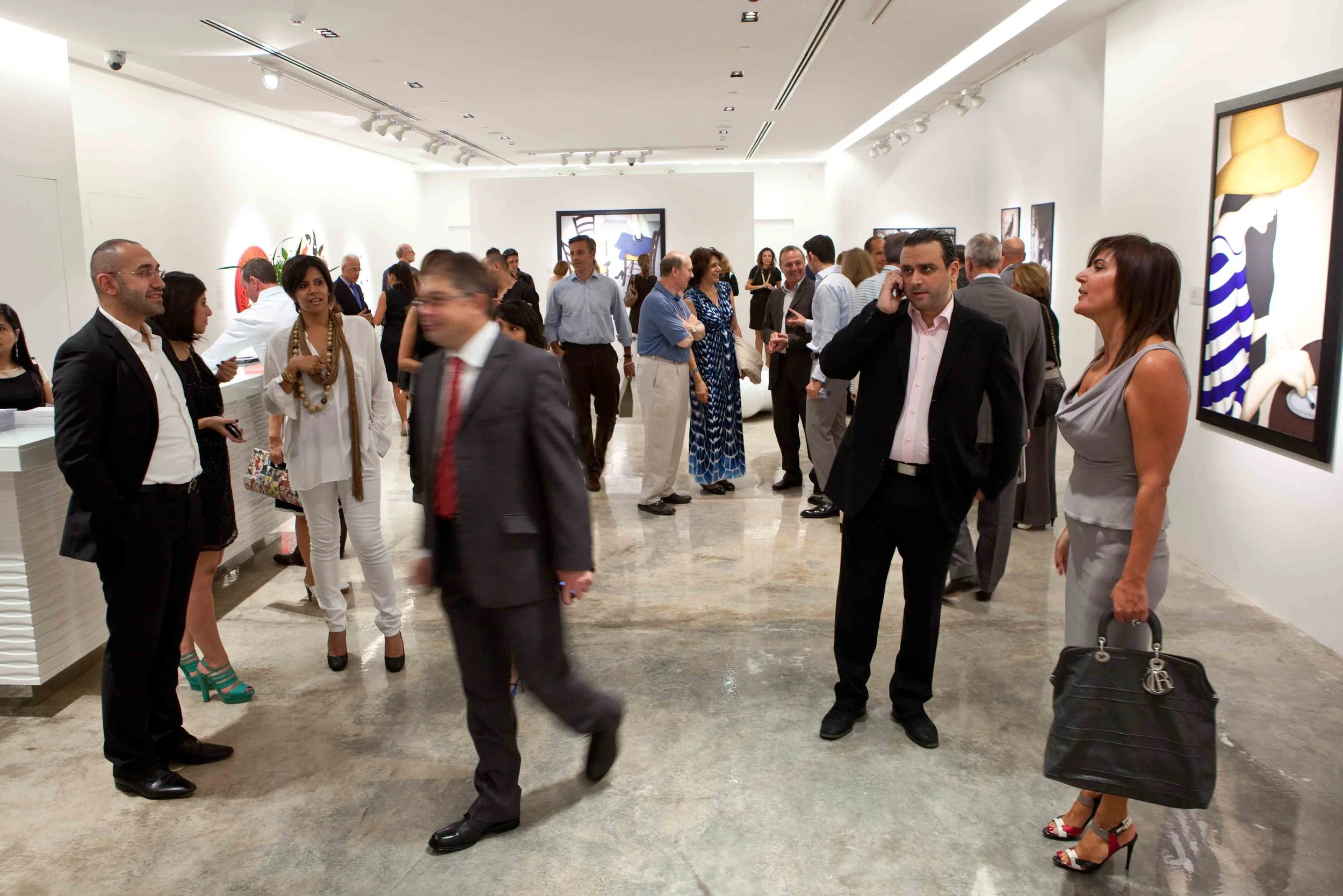 People gathered in an art gallery for an exhibition, viewing paintings and engaging in conversations.