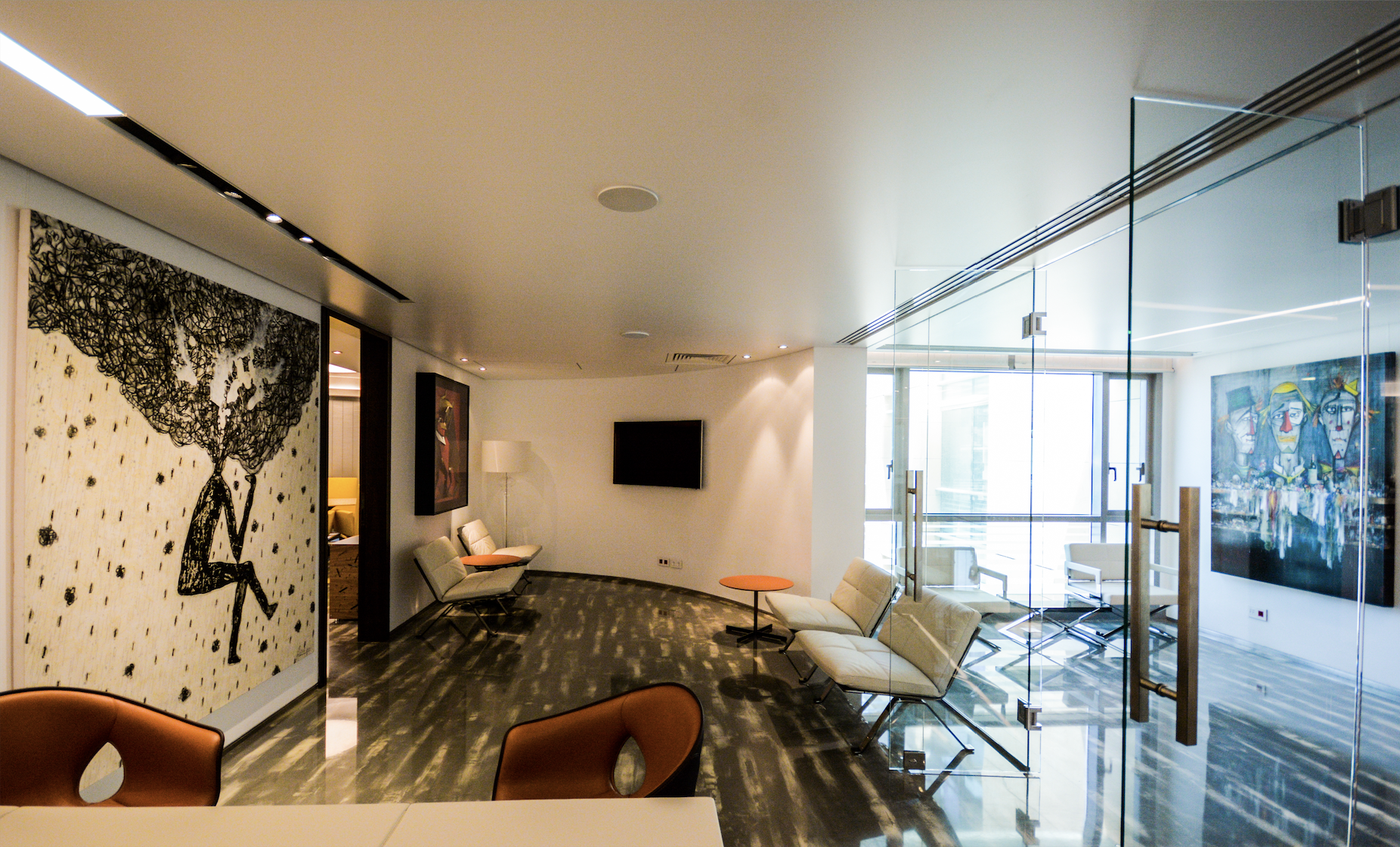 Modern hotel lobby with white walls, large window, contemporary art, and seating area with beige chairs and small orange tables.