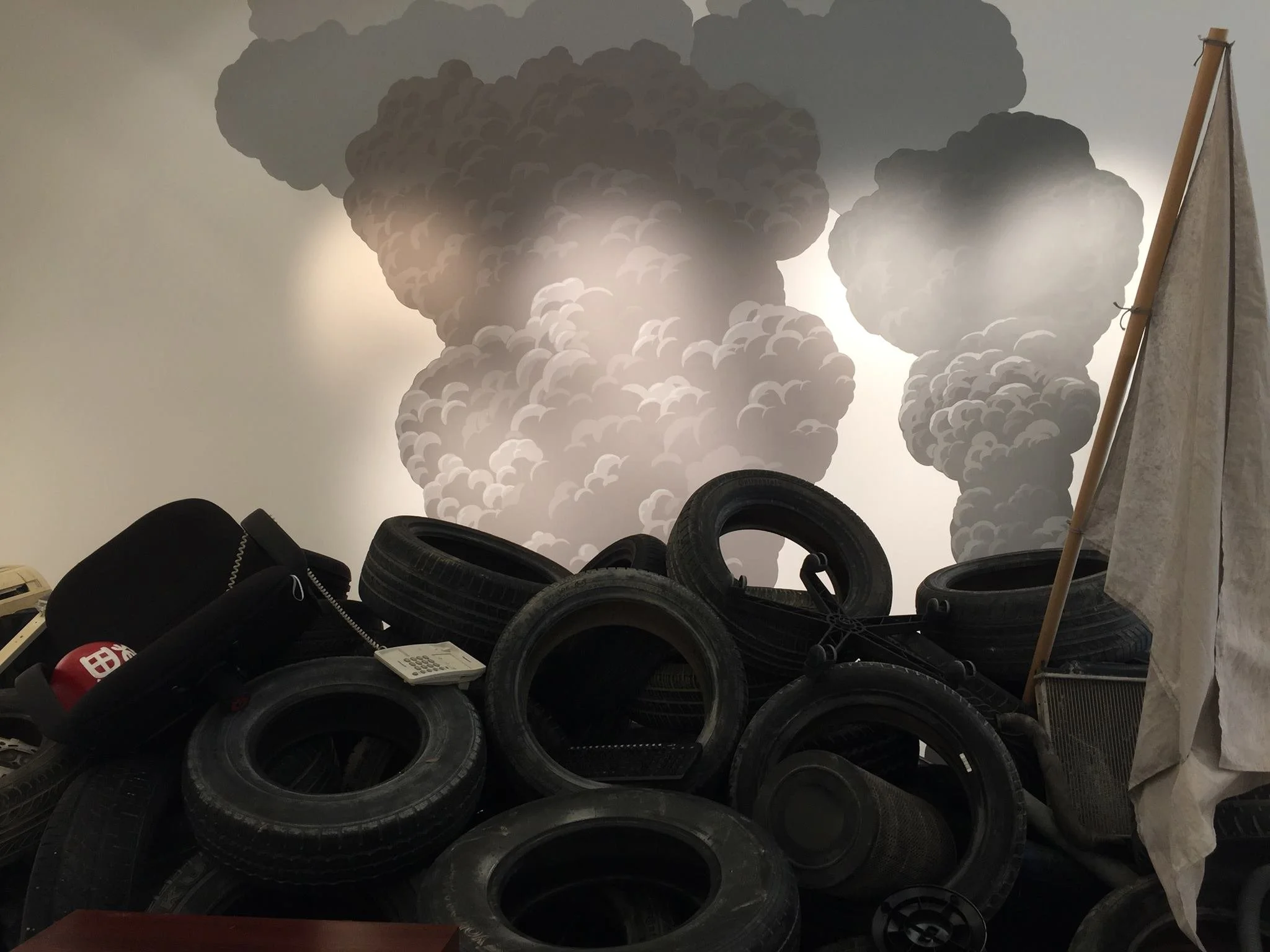A pile of black tires stacked in front of a wall with a large mural of smoke clouds.