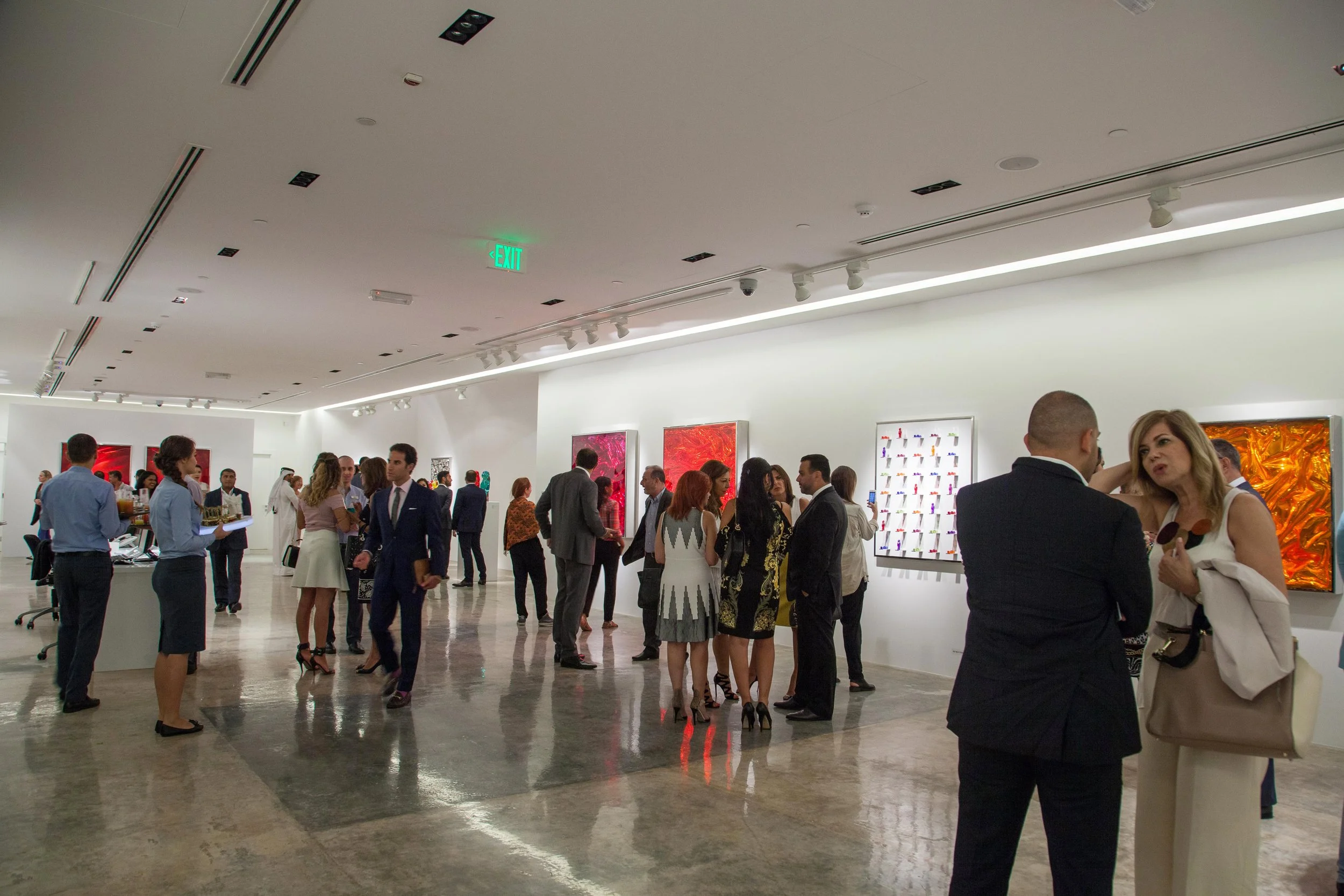 People attending an art exhibition in a gallery, looking at various colorful artworks on the walls.