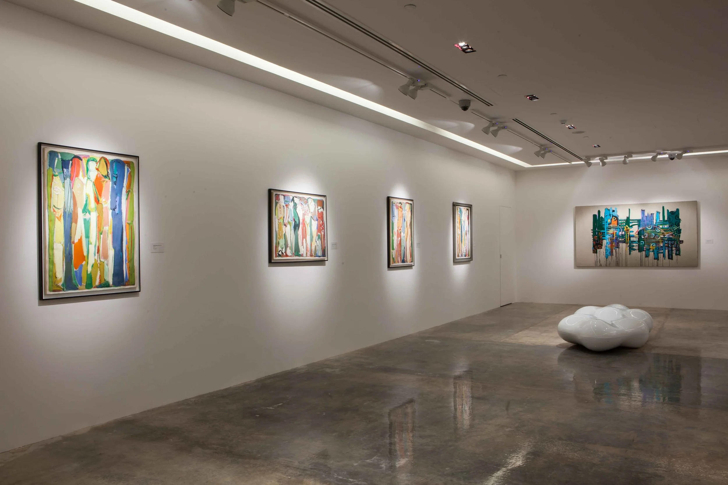 An art gallery with white walls and a concrete floor. There are five colorful abstract paintings on the wall and a modern white sculptural bench in the center of the room.