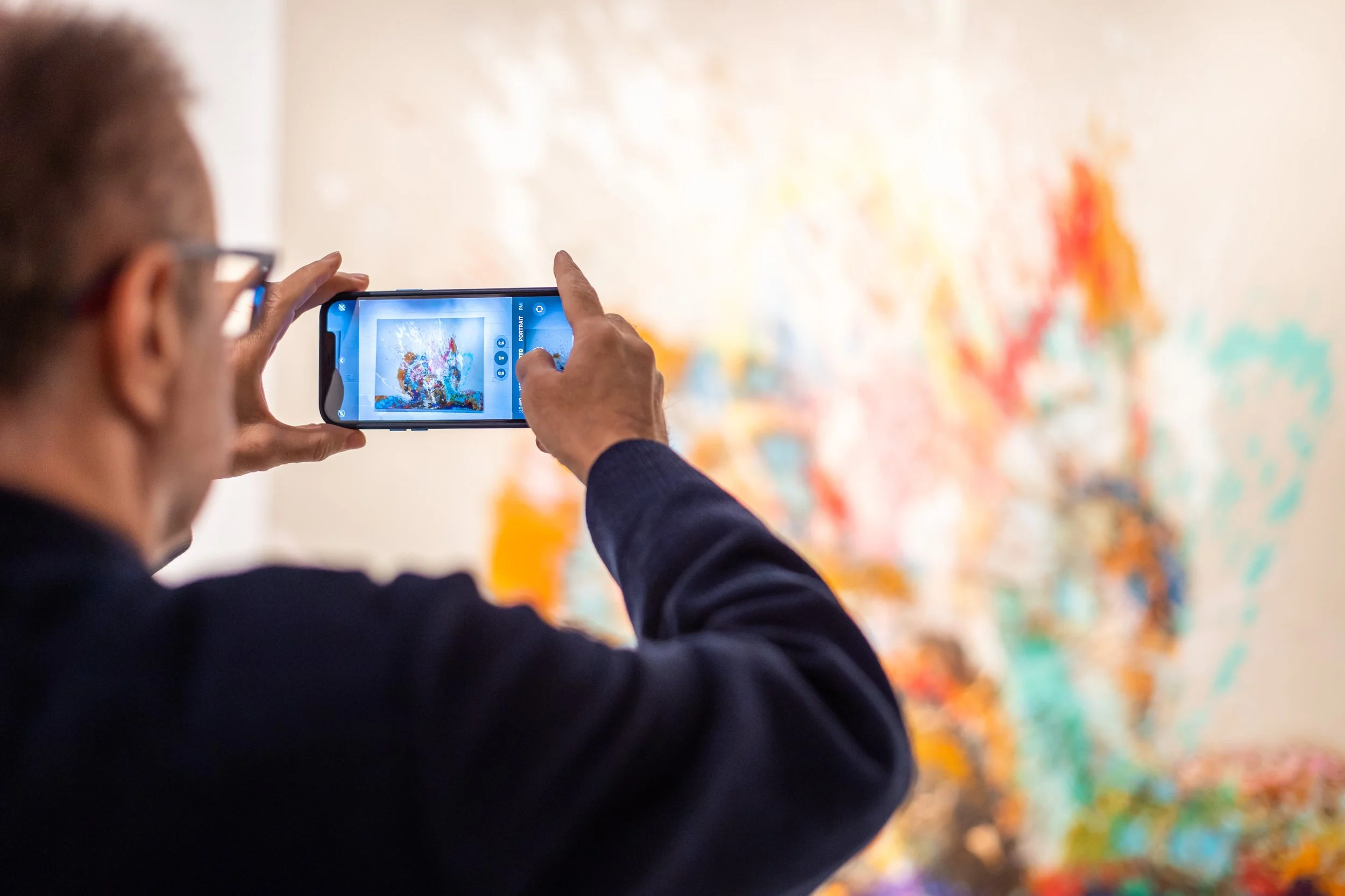 Person taking a photo of an abstract colorful painting with a smartphone.