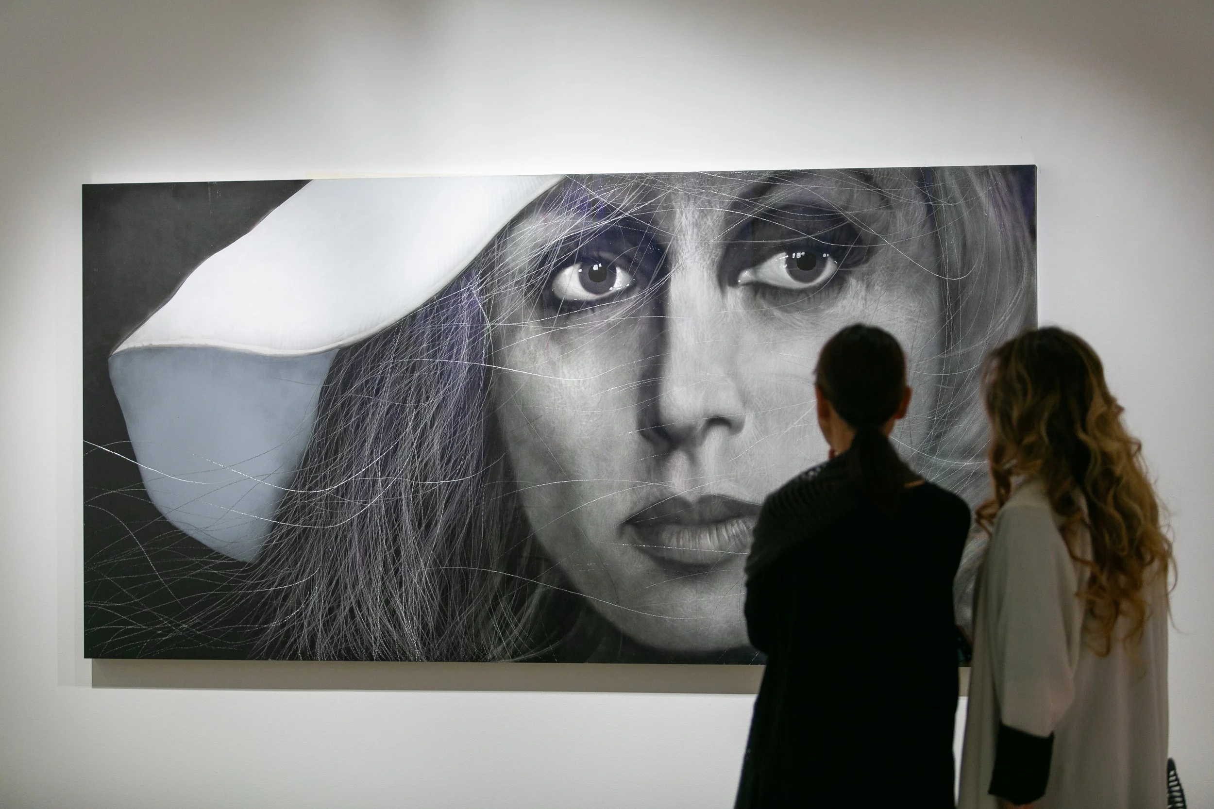 Two women viewing a large black and white portrait of a woman's face at an art gallery.