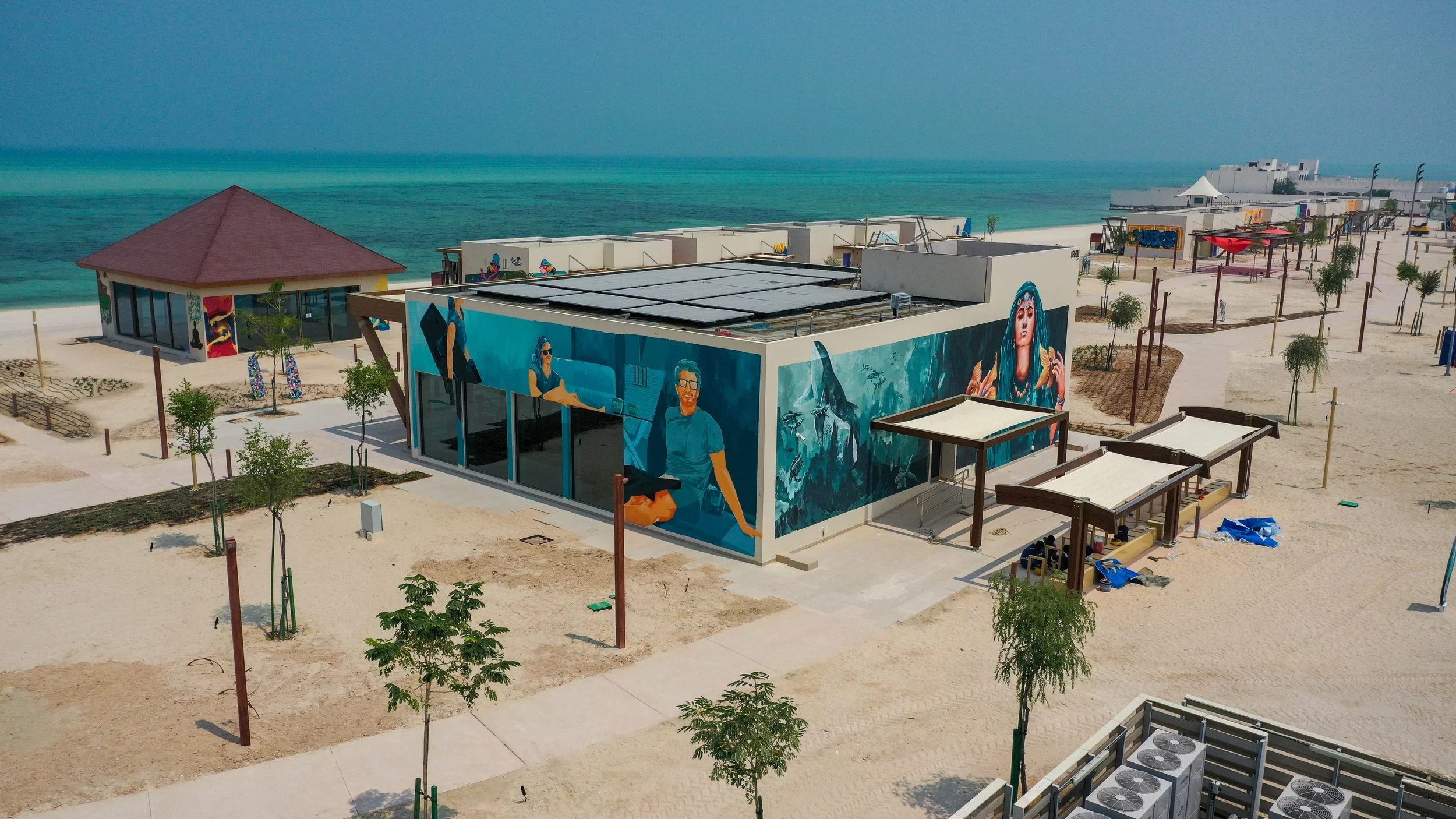 Beachside mural depicting diverse women, with the ocean in the background and a modern building in the foreground.
