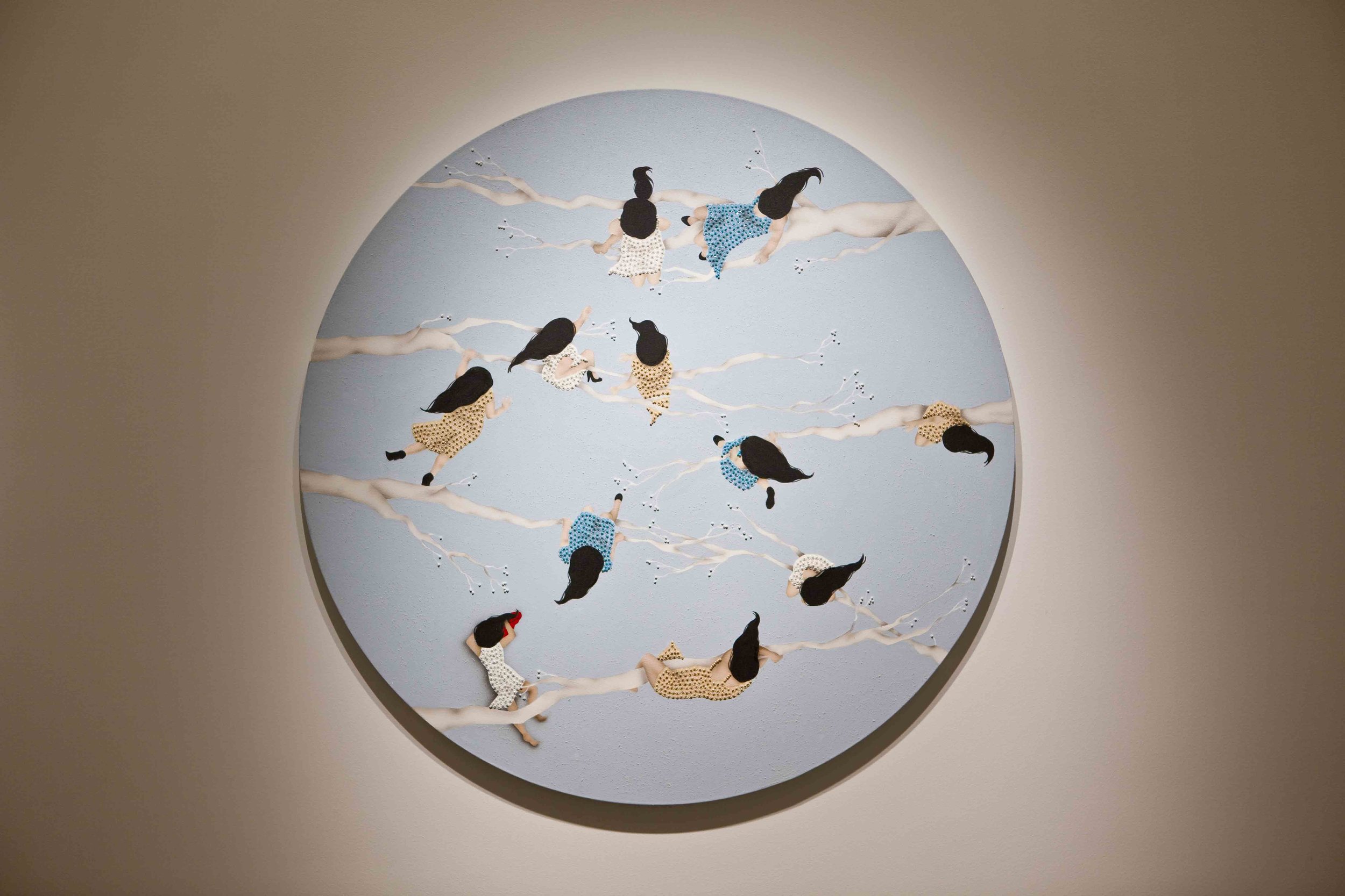 Wall art depicting children in polka dot dresses and shorts climbing and sitting on white tree branches against a blue circular background.