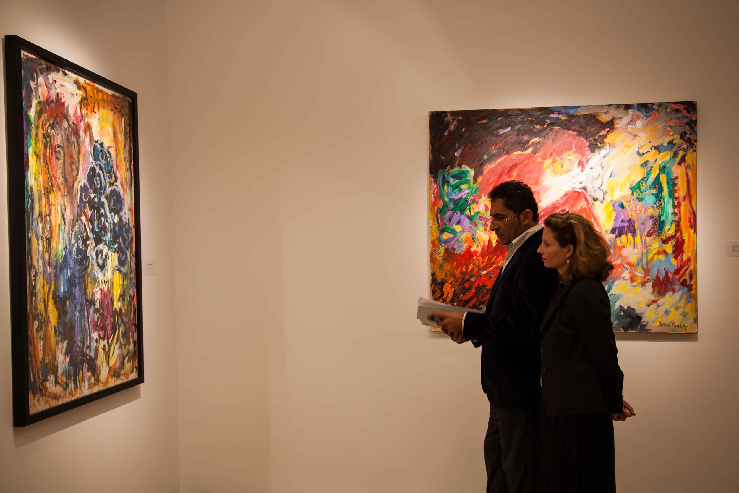 Two people, a man and a woman, standing in an art gallery, observing colorful abstract paintings on the wall.