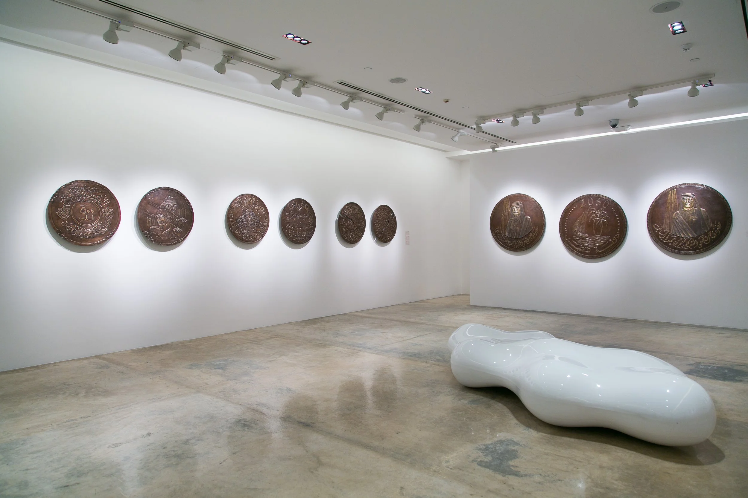 Art gallery with wall-mounted large round bronze coins and a modern white sculptural bench.