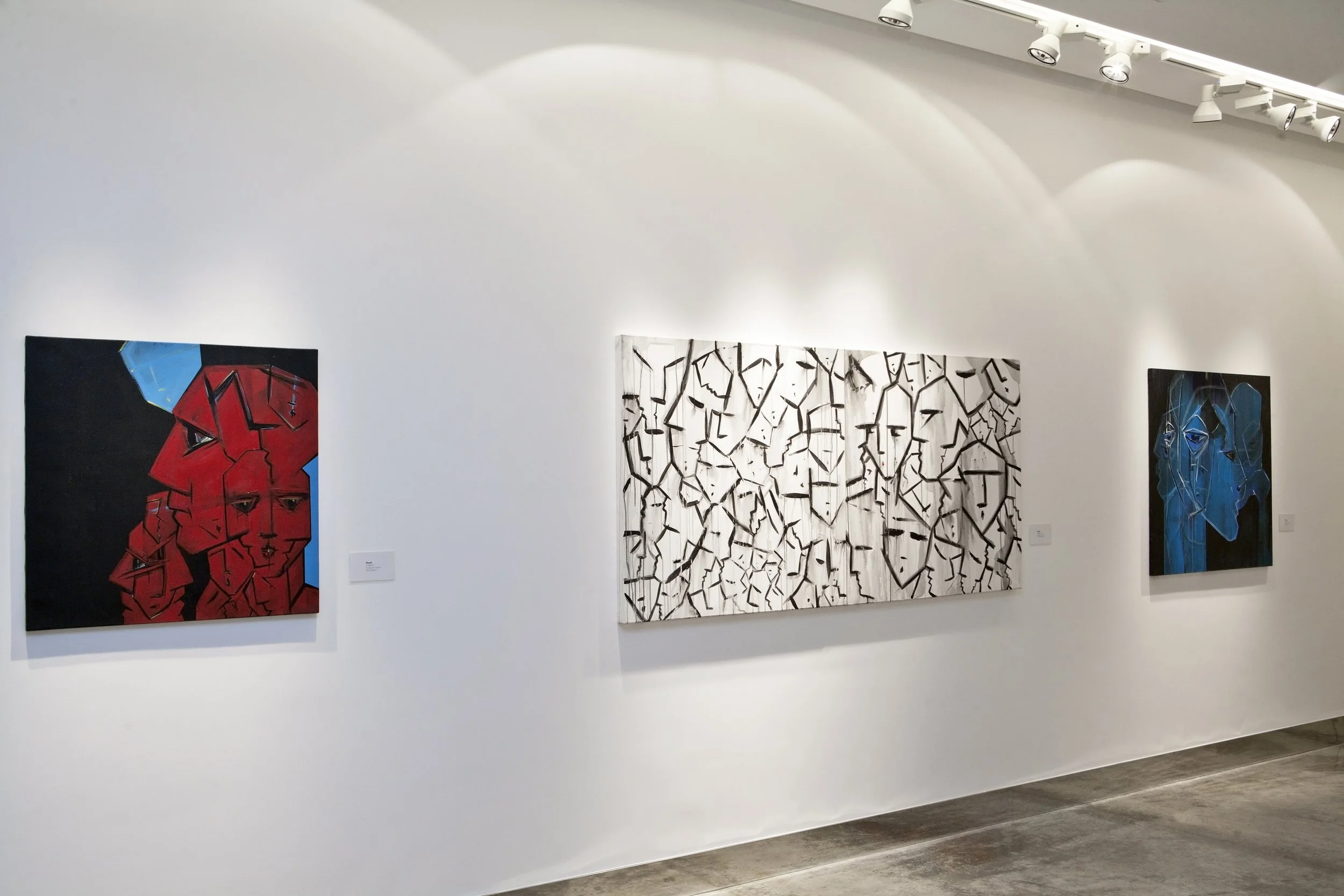 Paintings displayed on a white gallery wall, including abstract portraits and geometric designs, in a modern art exhibition.